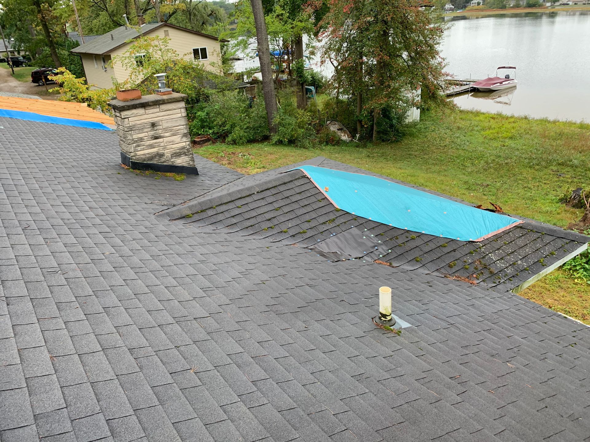 Rooftop with gray shingles, blue solar panel sections, chimney, and lakefront view in the background