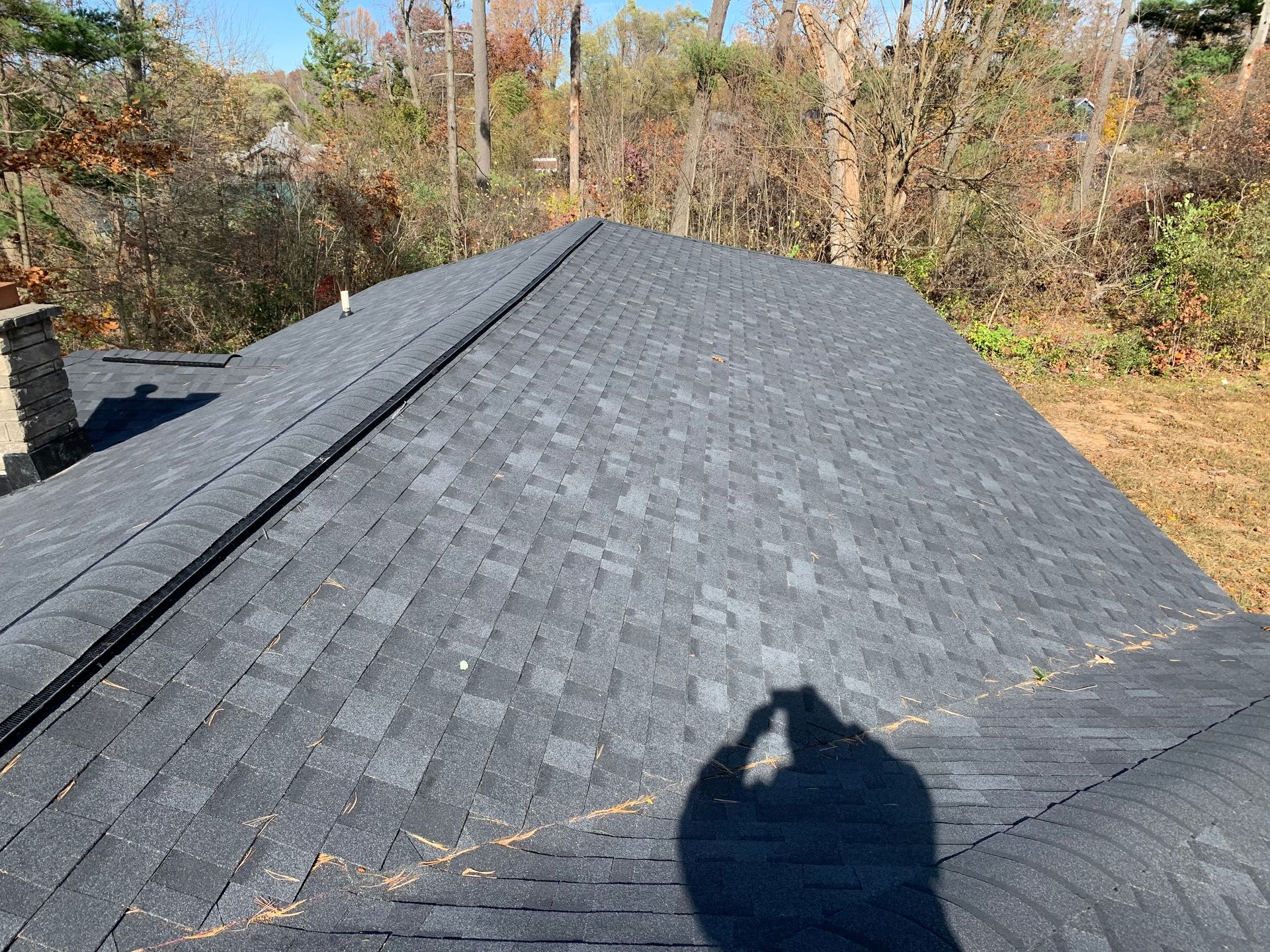 Dark gray shingle roof on a house, with trees and yard in the background