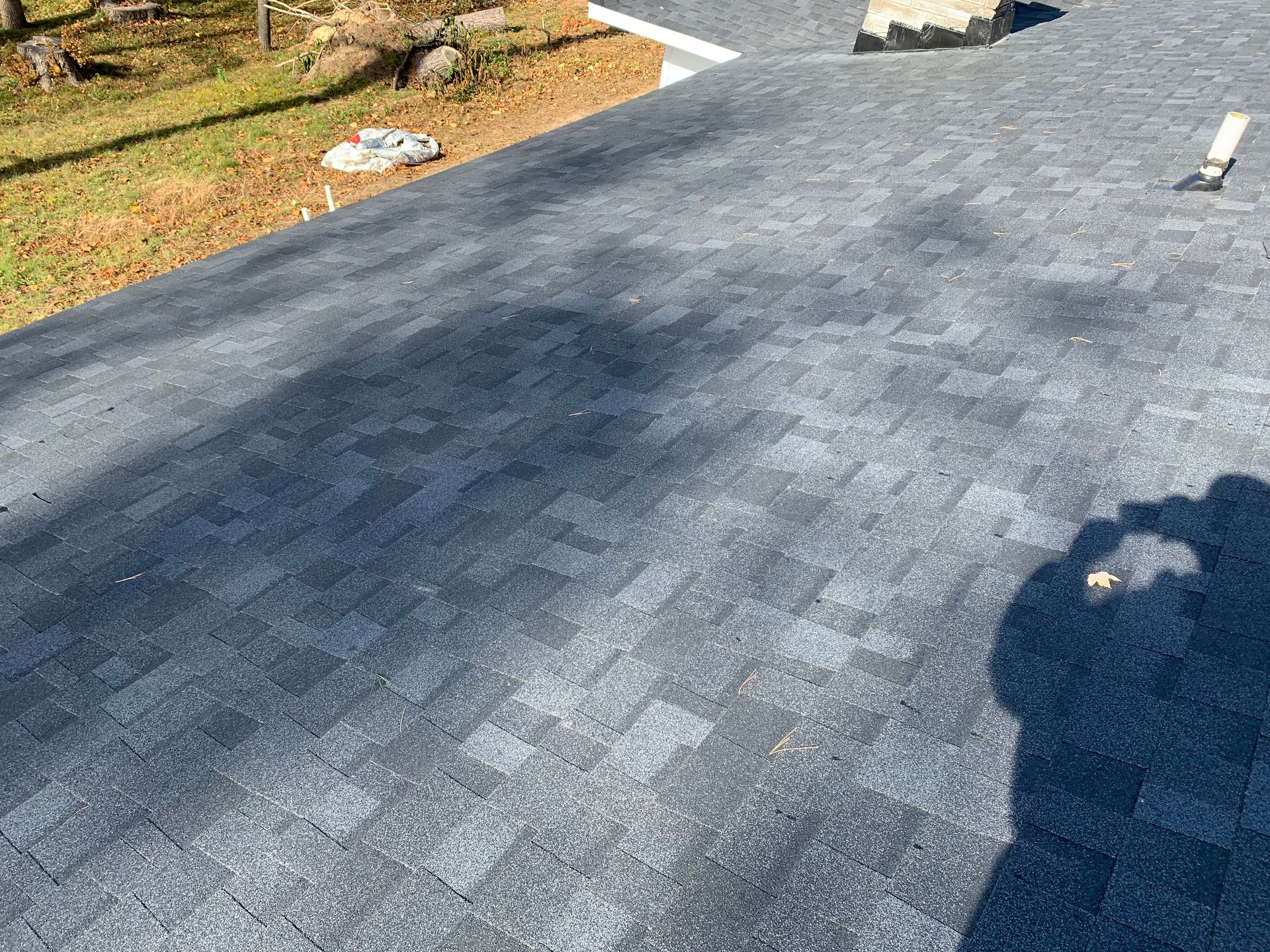 Freshly paved asphalt driveway with a shadow in the foreground and grass along the edge