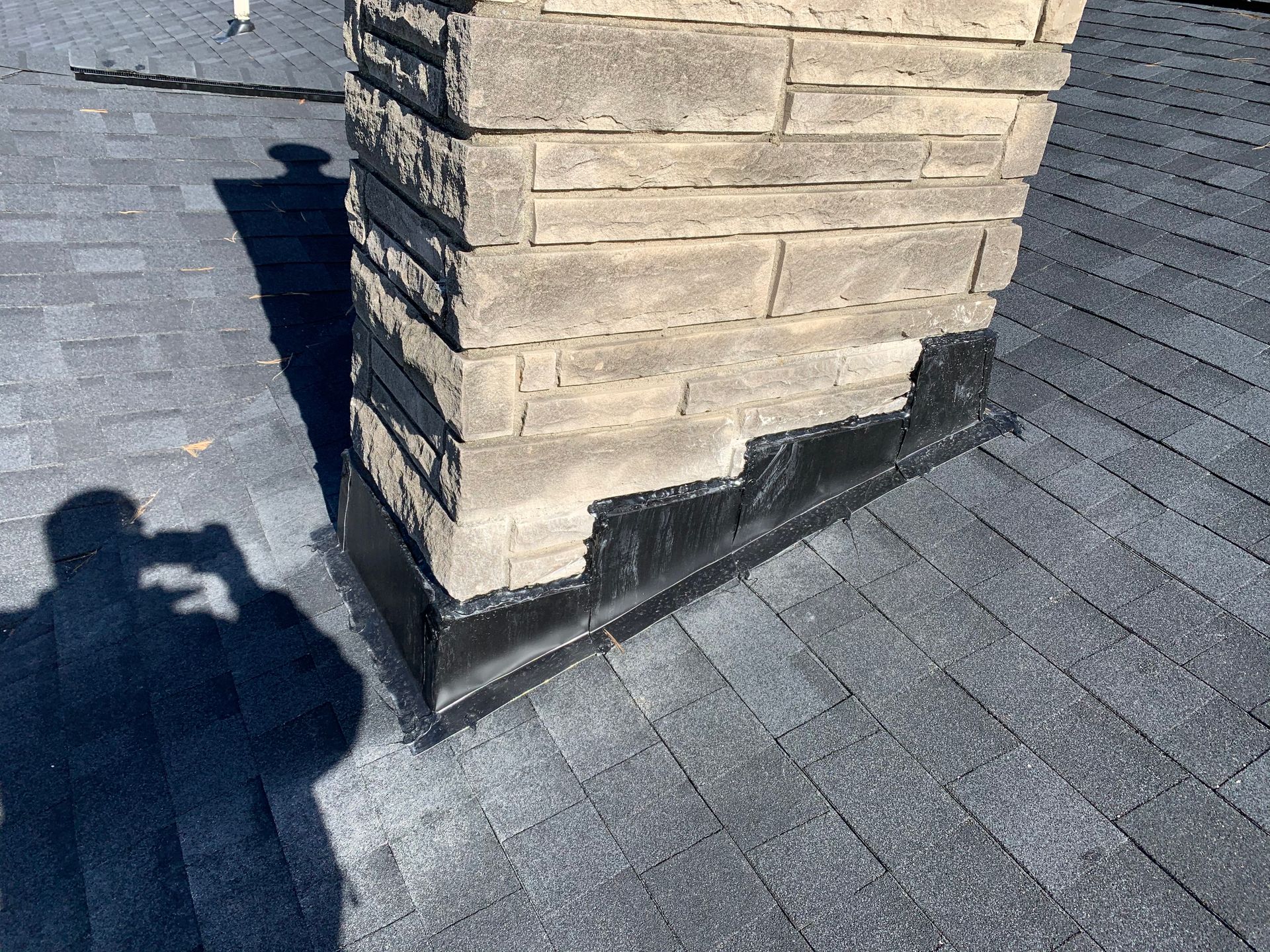 Brick chimney on a shingled roof with a visible shadow in sunlight