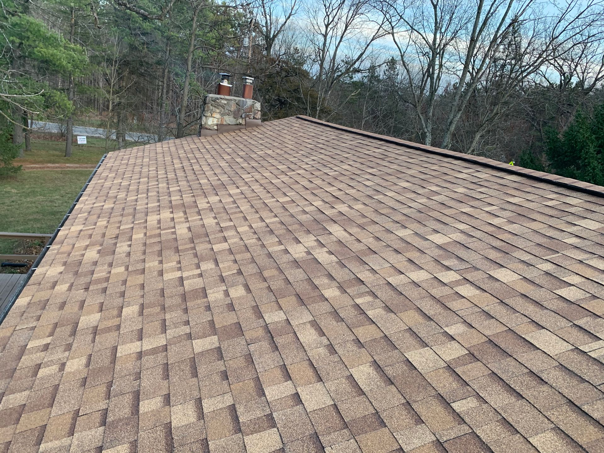 Tan shingled roof on a house with trees and yard in the background