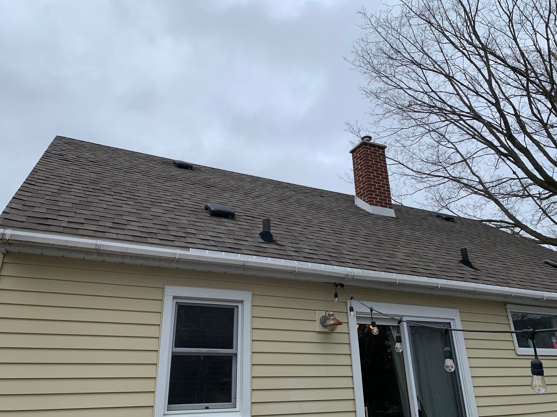House roof damaged by storm, with missing shingles and an open window below.