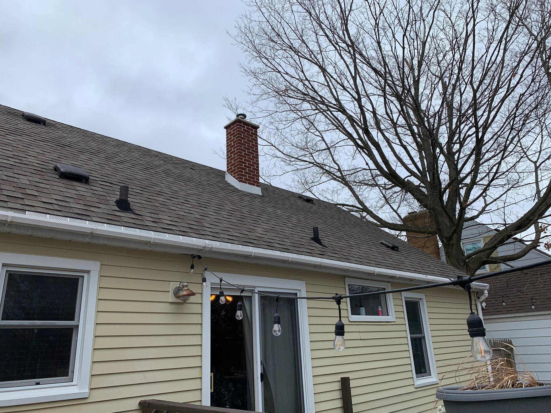 Back of a beige house with a chimney, open patio door, and bare tree in winter
