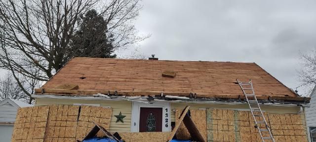 Partially roofed house under construction with plywood walls and a ladder on the roof