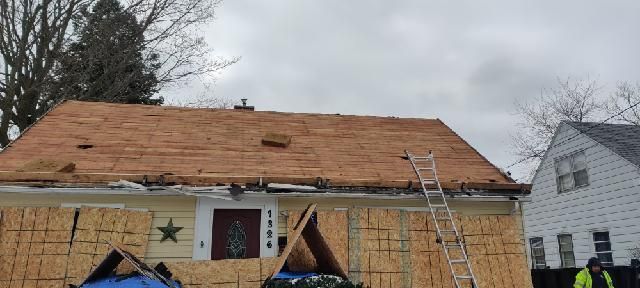 Workers repairing a house roof with ladders and a tarp over the front porch.