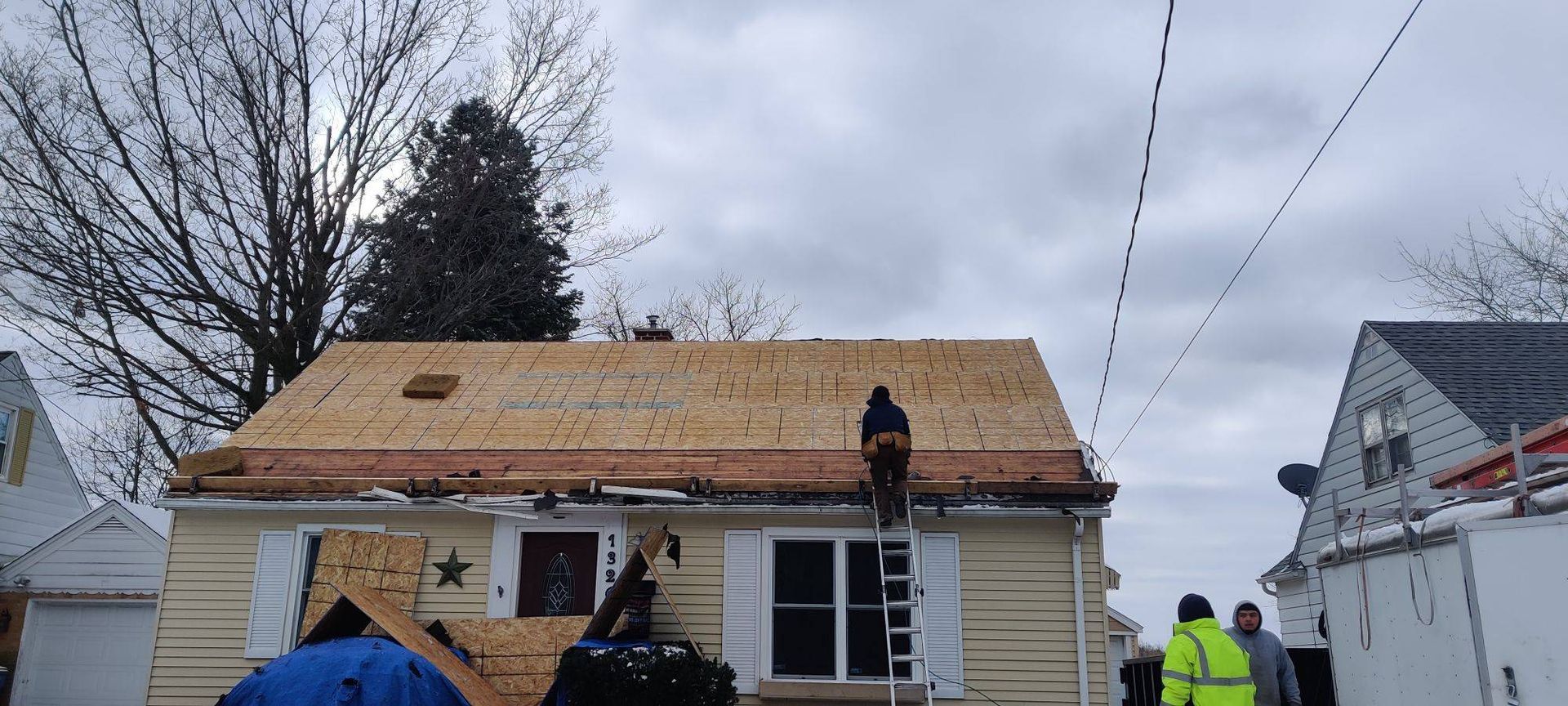 Workers repairing a house roof with exposed plywood on a cloudy day