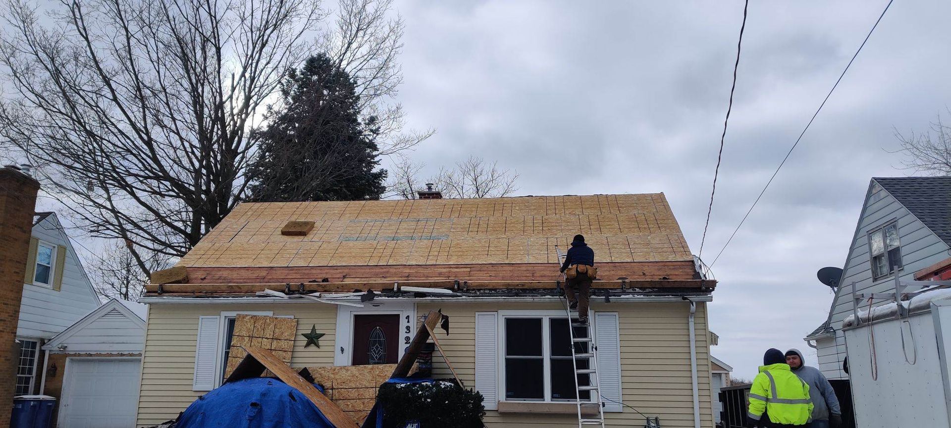 Workers reroofing a house with exposed plywood roof and overcast sky