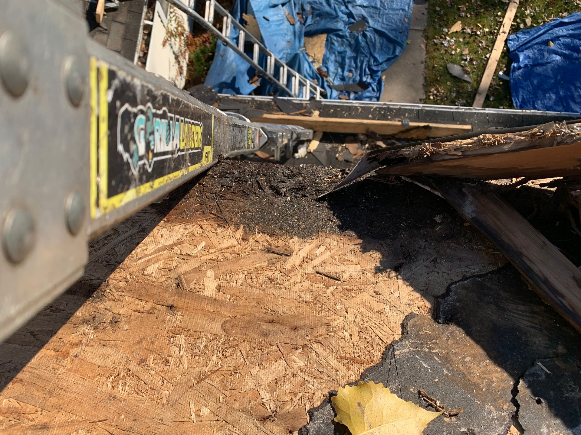 Construction equipment scraping dirt beside a blue tarp-covered area, with a muddy ground surface.