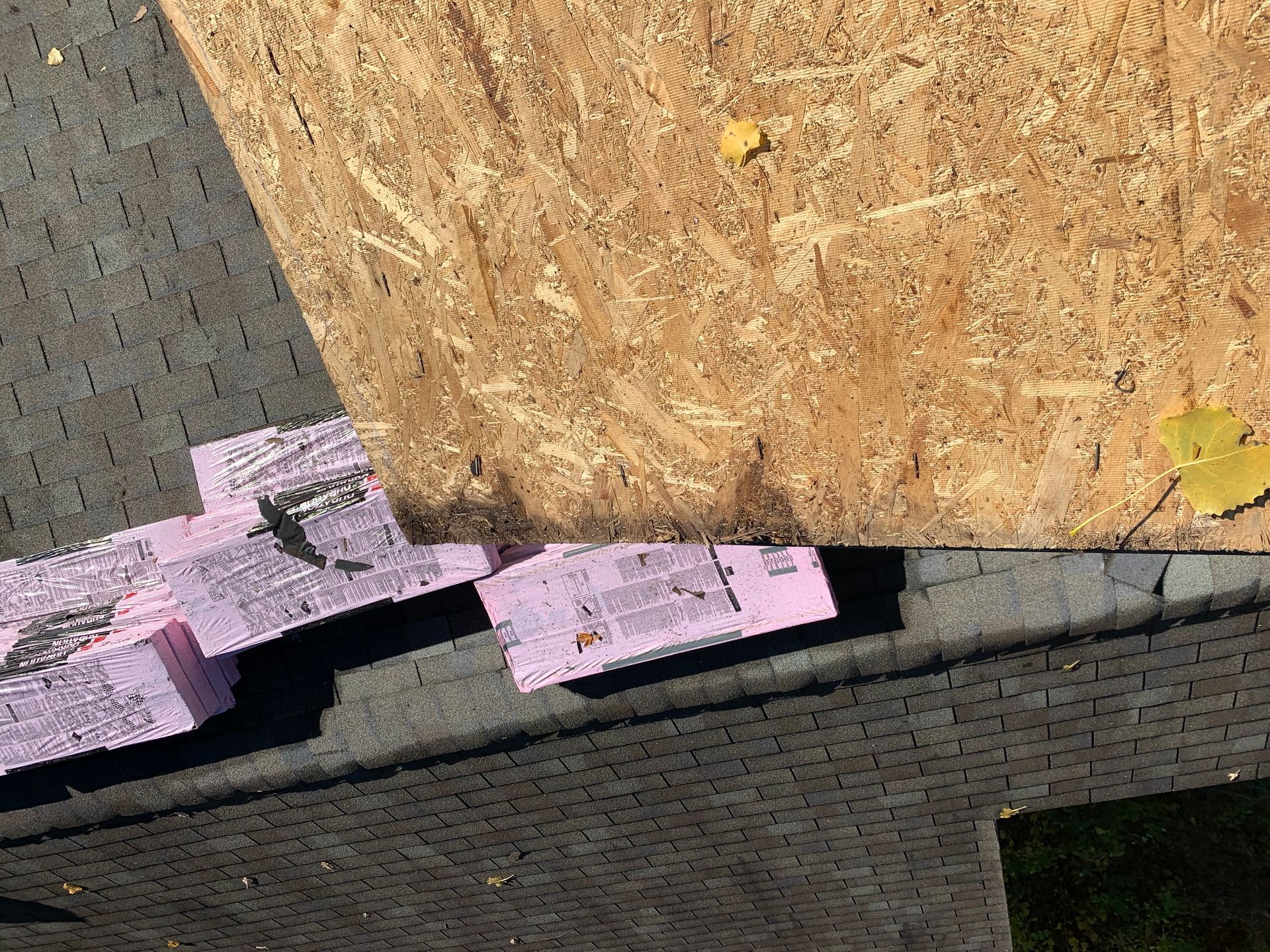 Pink foam insulation boards against a wooden wall and dark brick edge outdoors