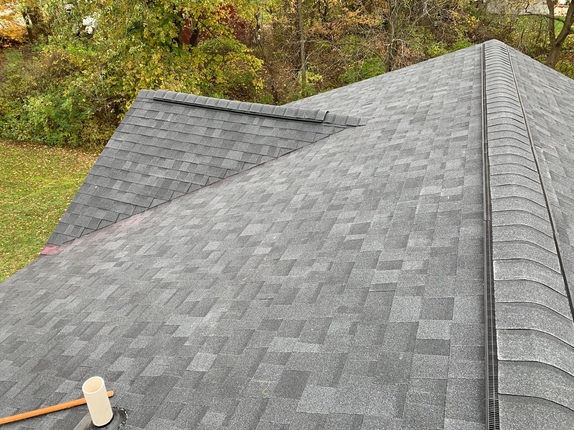 Gray shingled roof with a steep peak, viewed from above, with trees and foliage in the background
