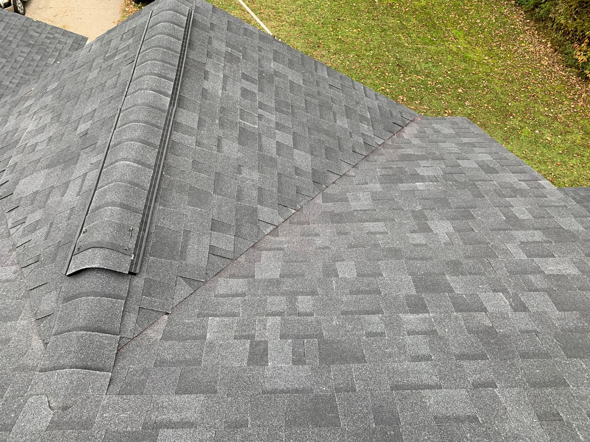 Gray asphalt shingle roof with a dormer vent and grassy edge in the background