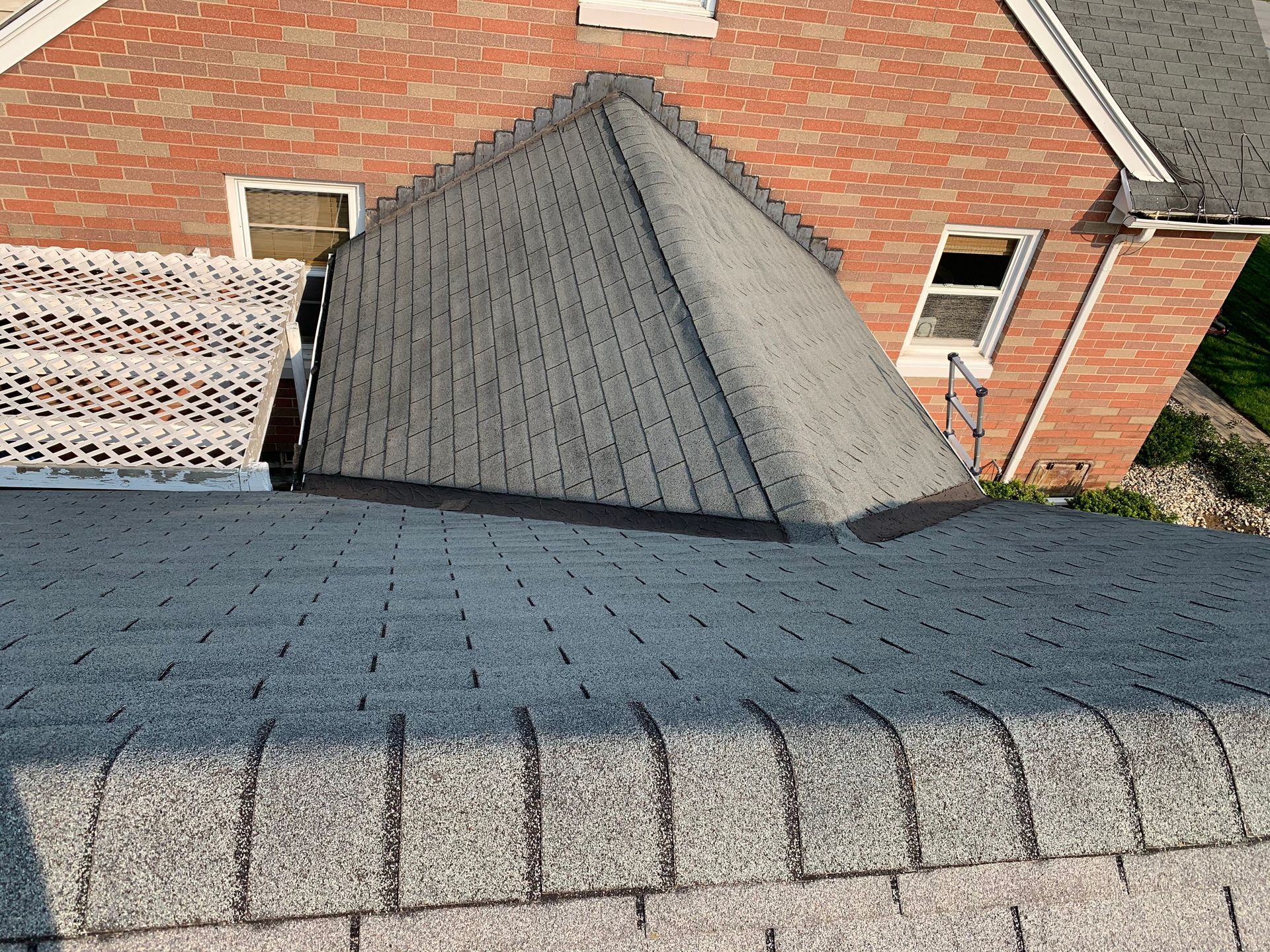 View from a roof showing a gray shingled dormer against red brick walls and a neighboring roofline.