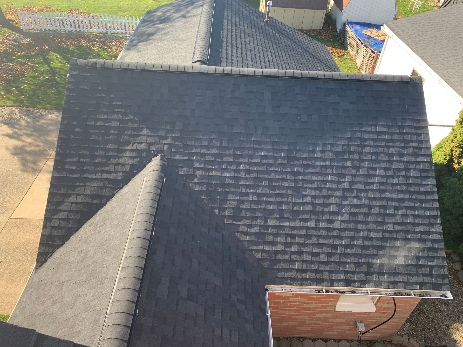 Aerial view of dark gray shingled house roofs with a small brick chimney and neighboring yards.
