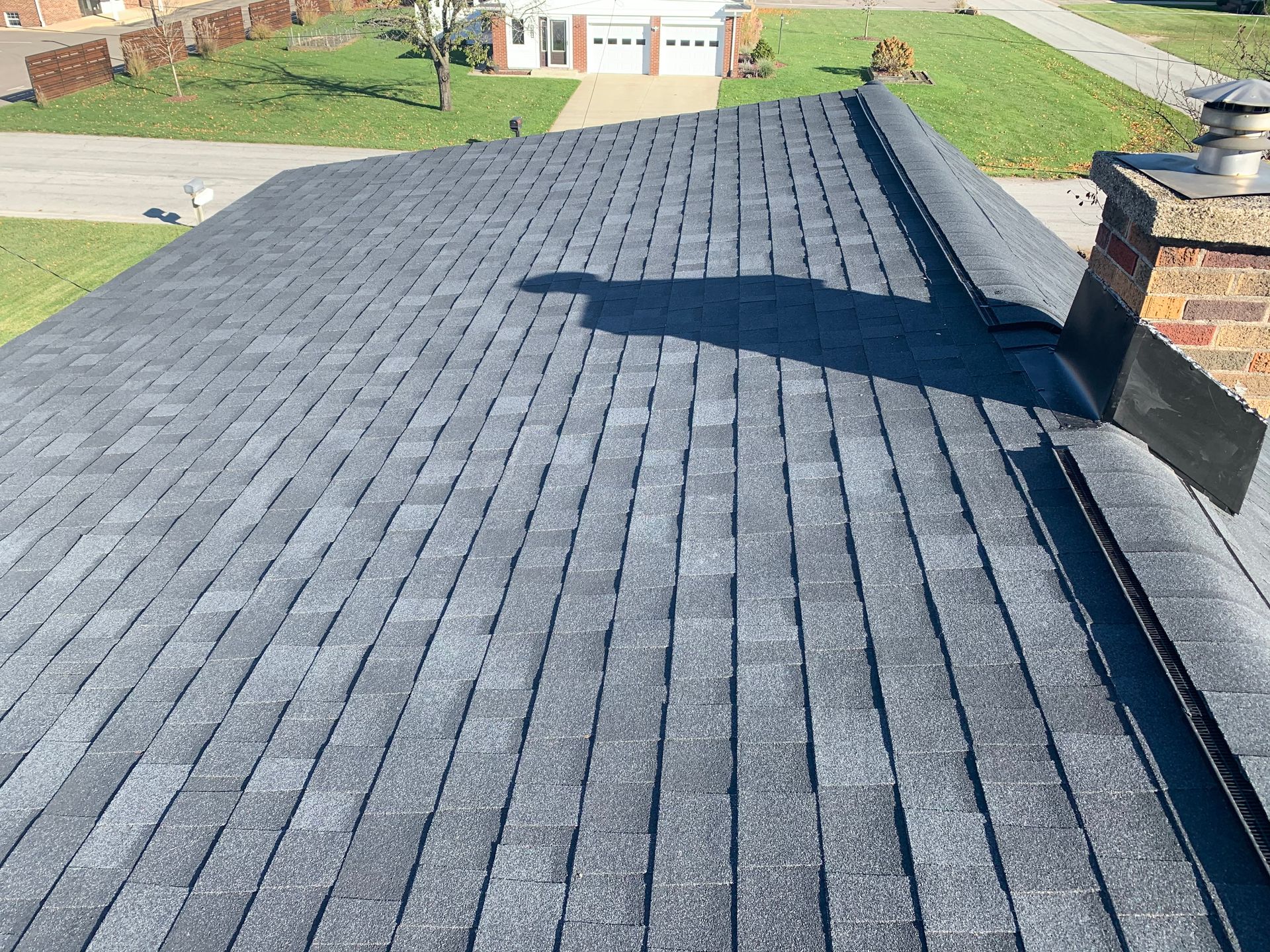 Dark gray shingled roof with a large shadow cast across it in daylight.