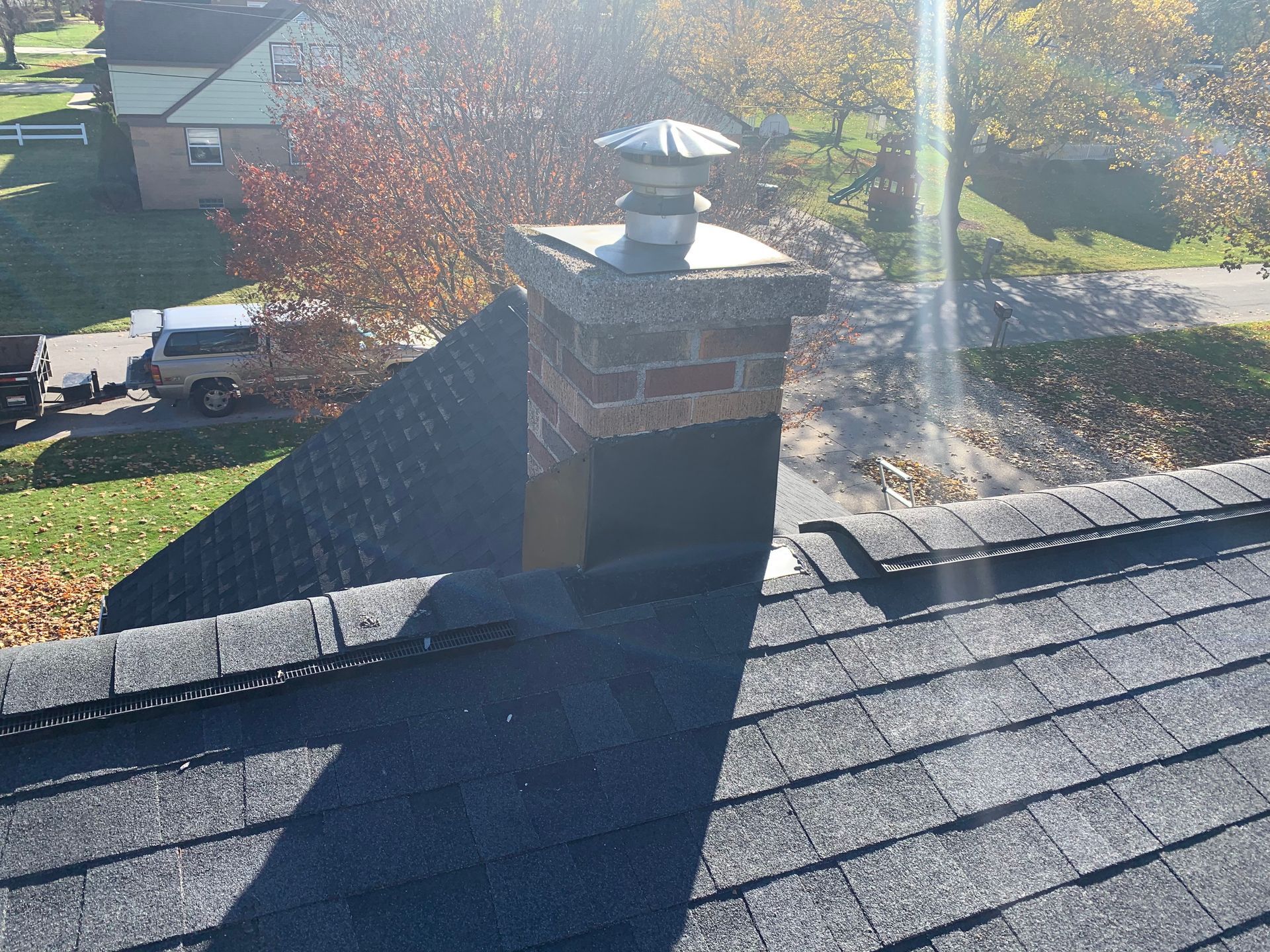 Rooftop chimney with metal cap and smoke, viewed over a residential neighborhood in bright sunlight