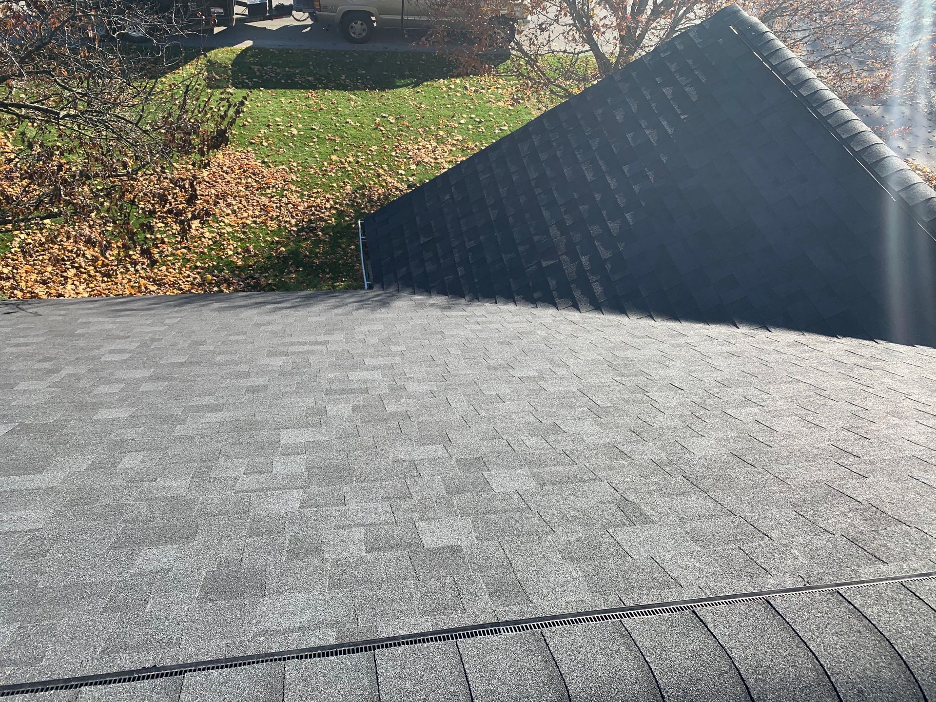 Gray shingled roof with a dark dormer and fallen autumn leaves in the background