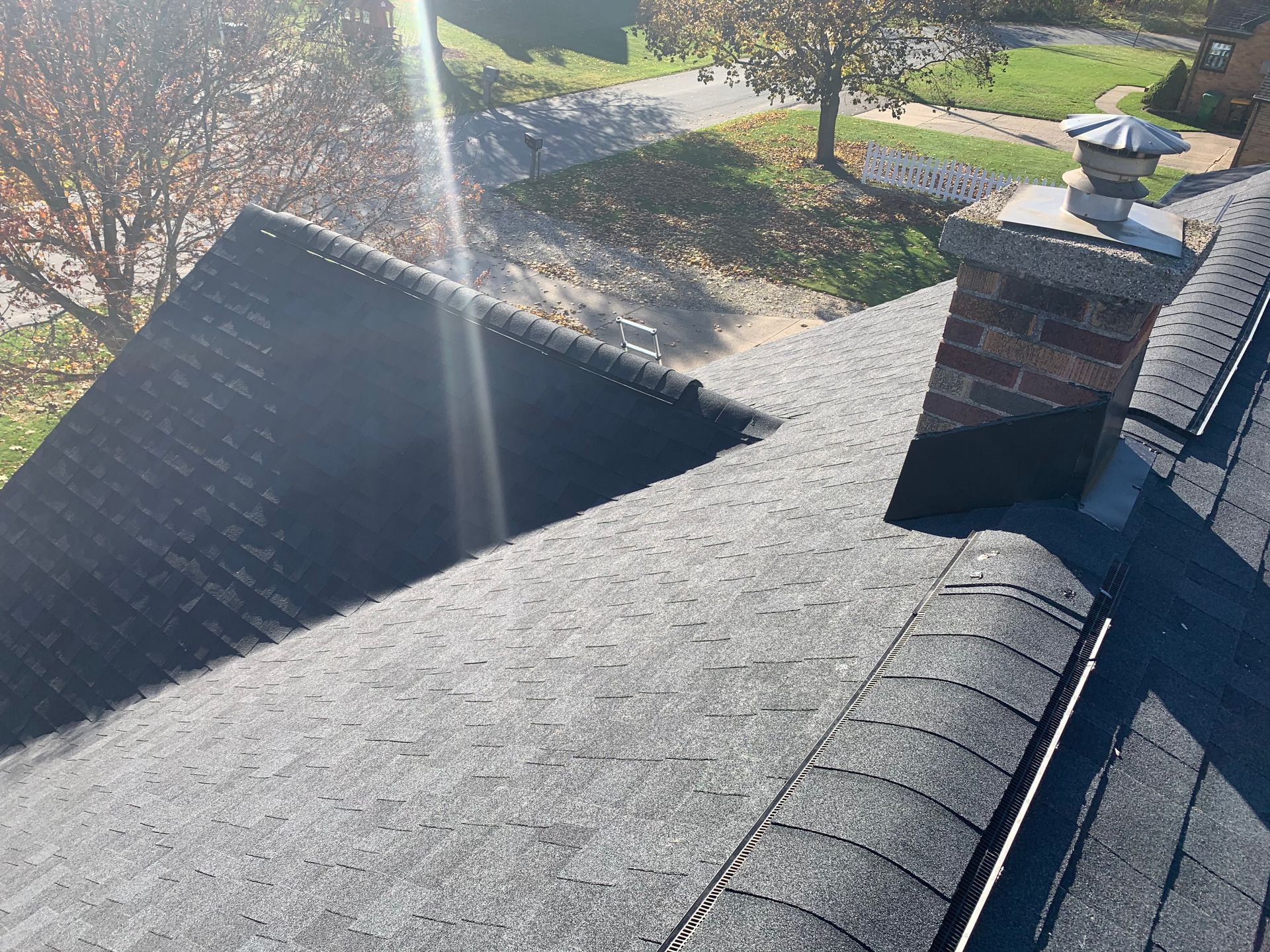 Roof shingles and chimney tops viewed from above in bright sunlight.