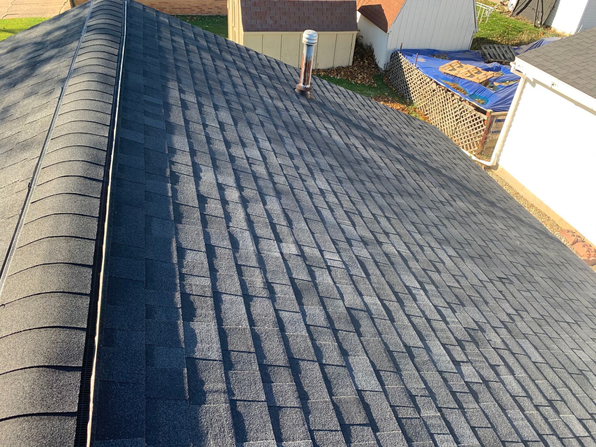 Rooftop view of gray shingles, with a person standing near the ridge and neighboring houses visible.