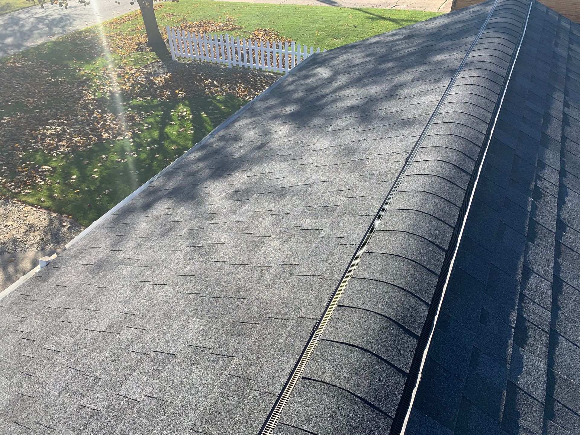 Weathered black roof shingles with a seam running along the ridge beside a yard and fence