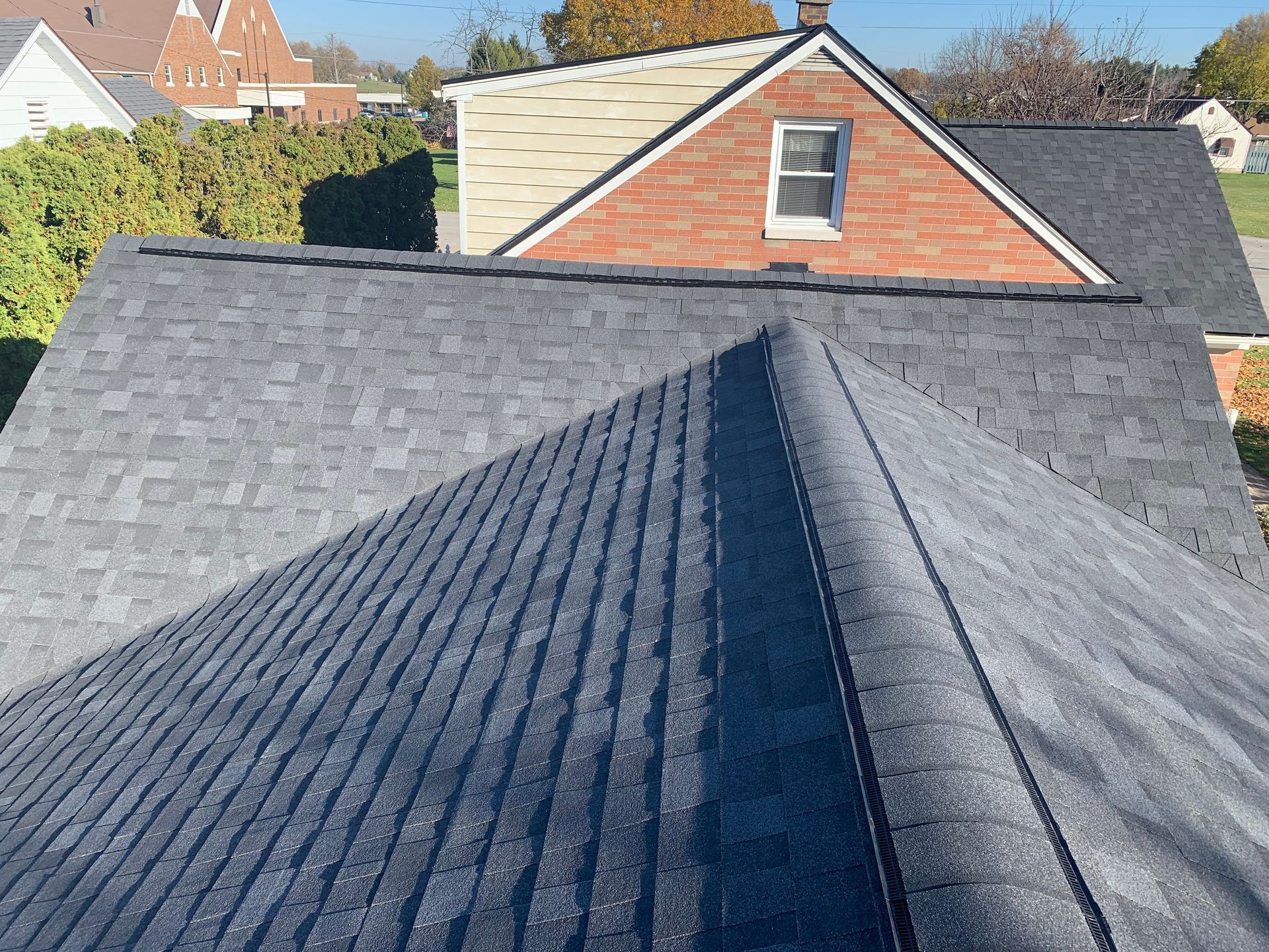Dark gray shingled roof with a central ridge, viewed toward neighboring houses and a red brick gable.