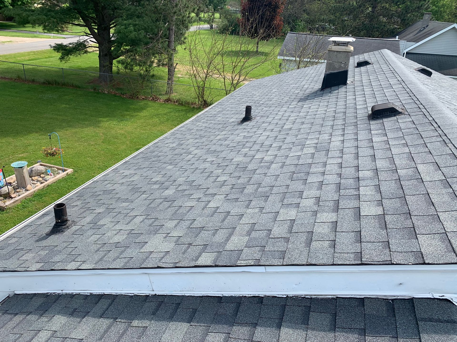 Roof with gray shingles and several vents, viewed from above beside a green yard