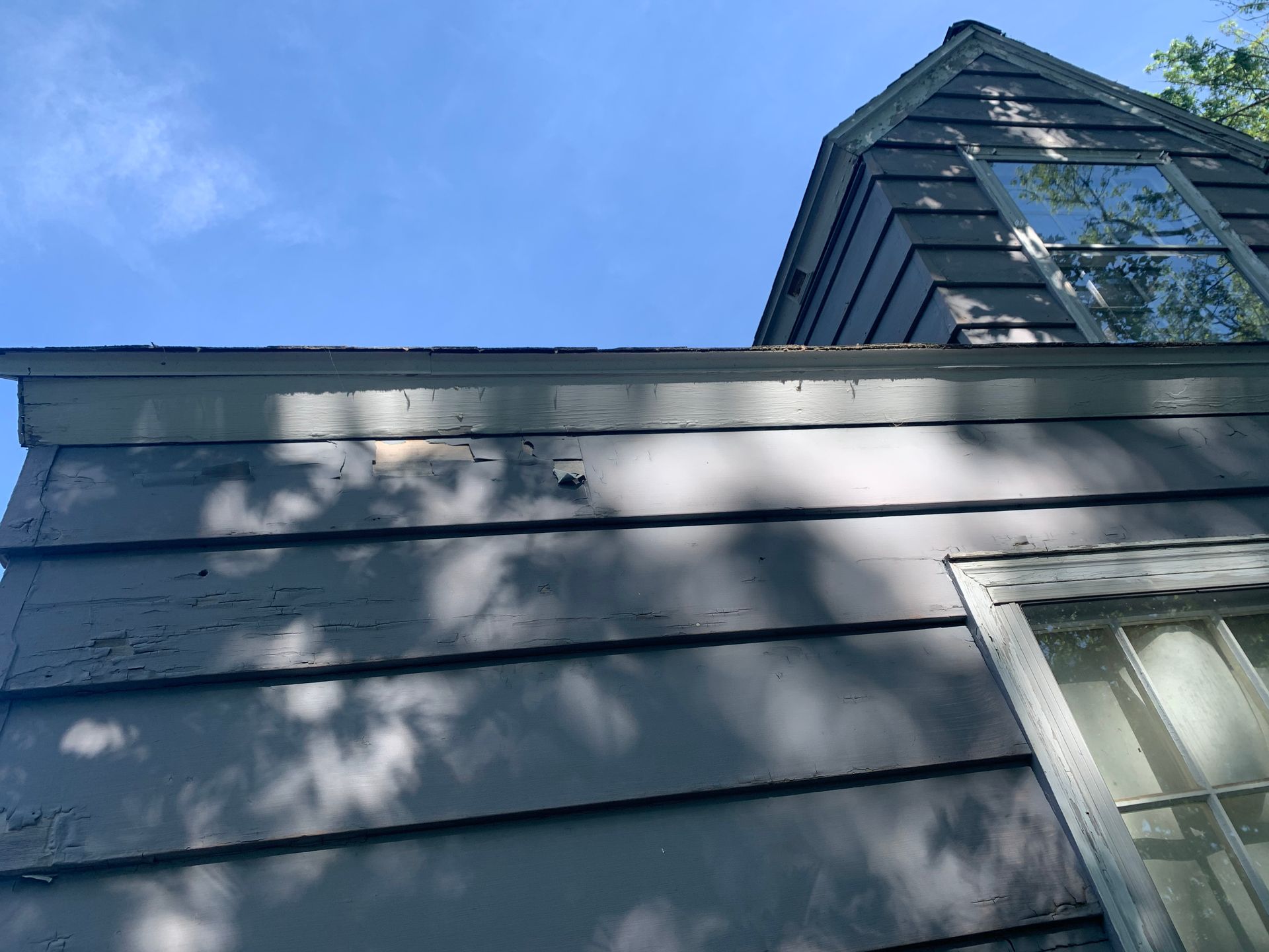 Blue-sided house with white-trimmed window and tower roof under a clear sky
