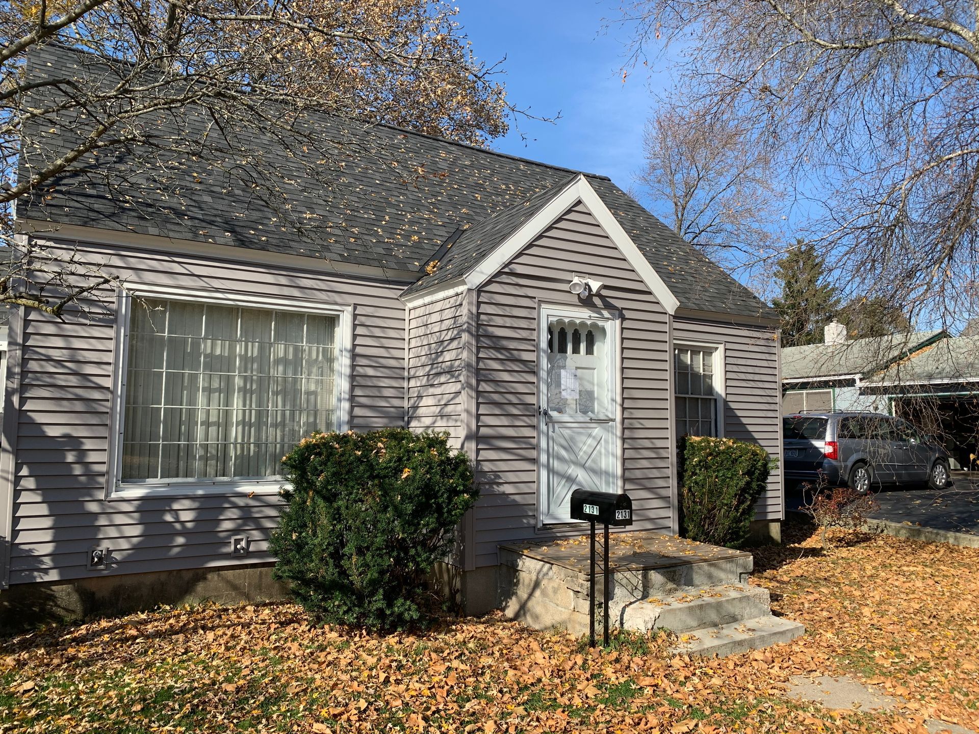 Small gray house with white trim, front steps, mailbox, and autumn leaves in the yard