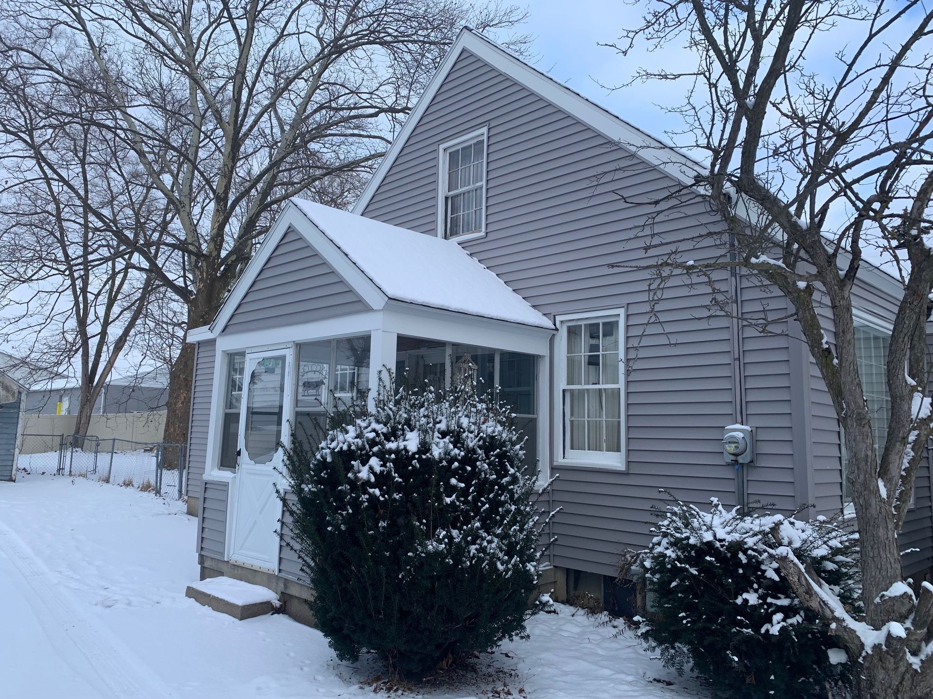 Snow-covered gray house with white trim and bare trees in winter