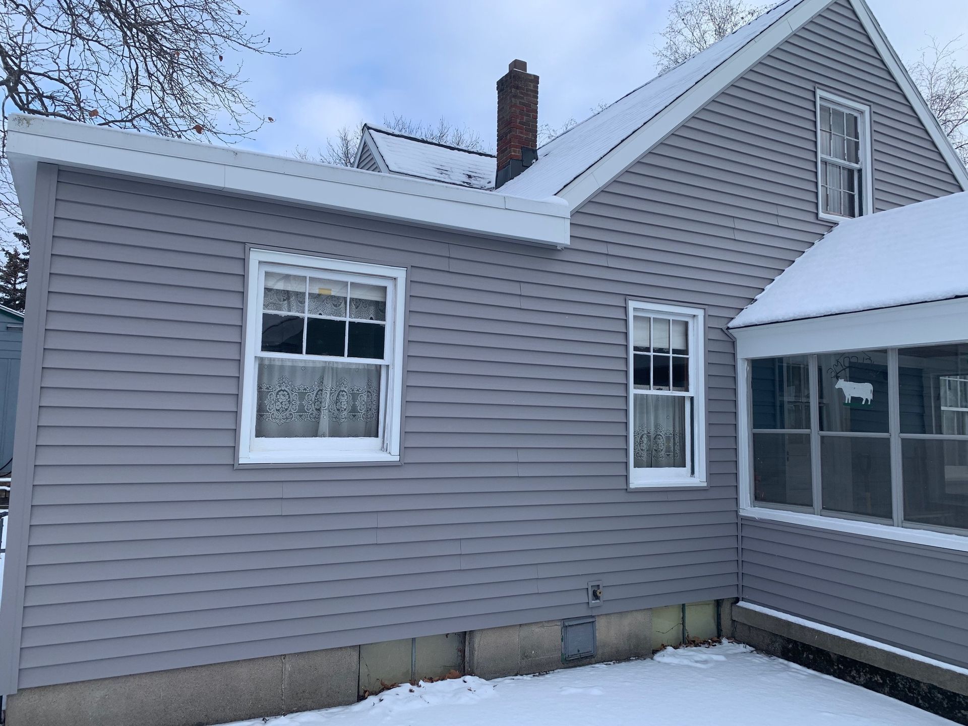 Gray house exterior with white trim and snow on the roof, seen in winter.