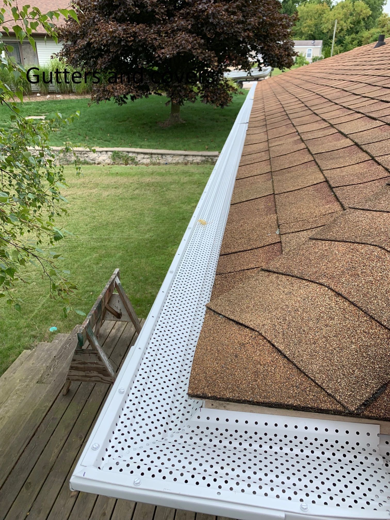 White metal gutter along a brown shingle roof edge above a backyard lawn.