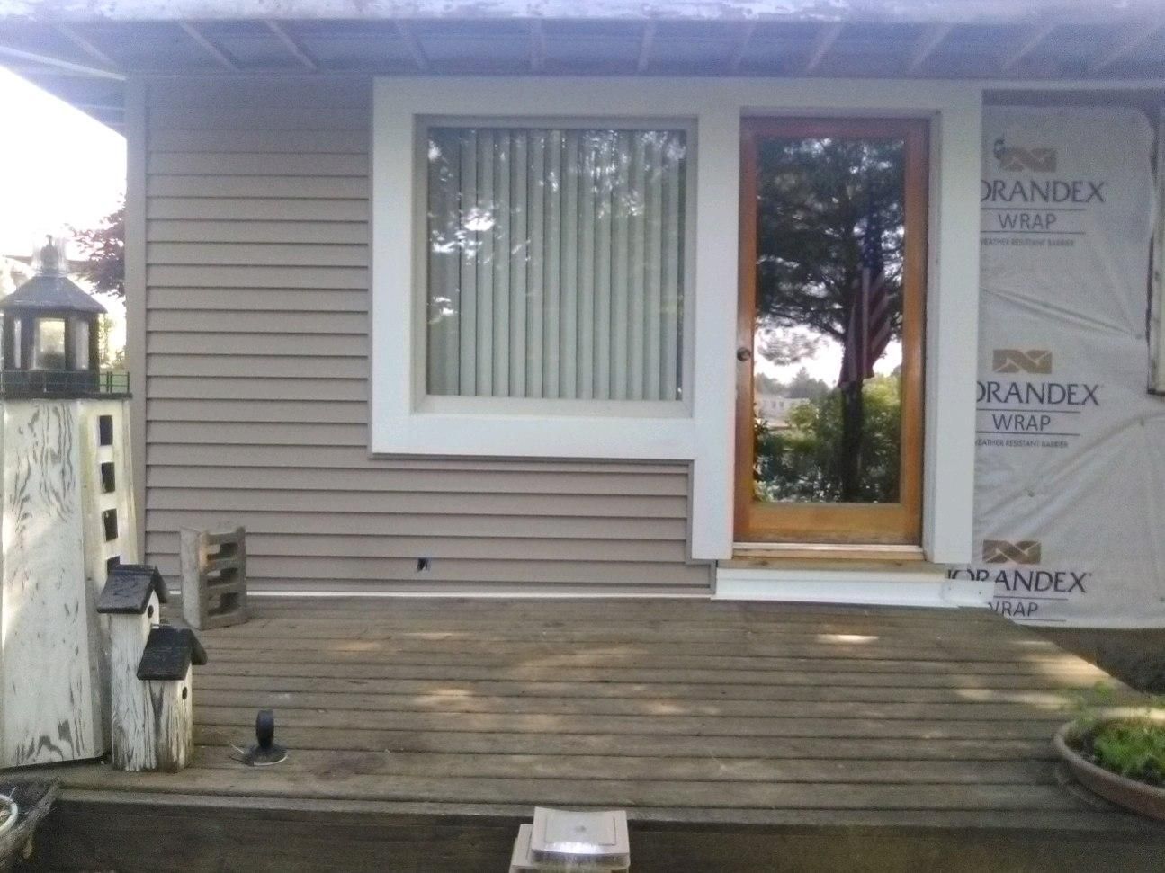 Back porch with wooden deck, front door, window, and partially finished siding on the right