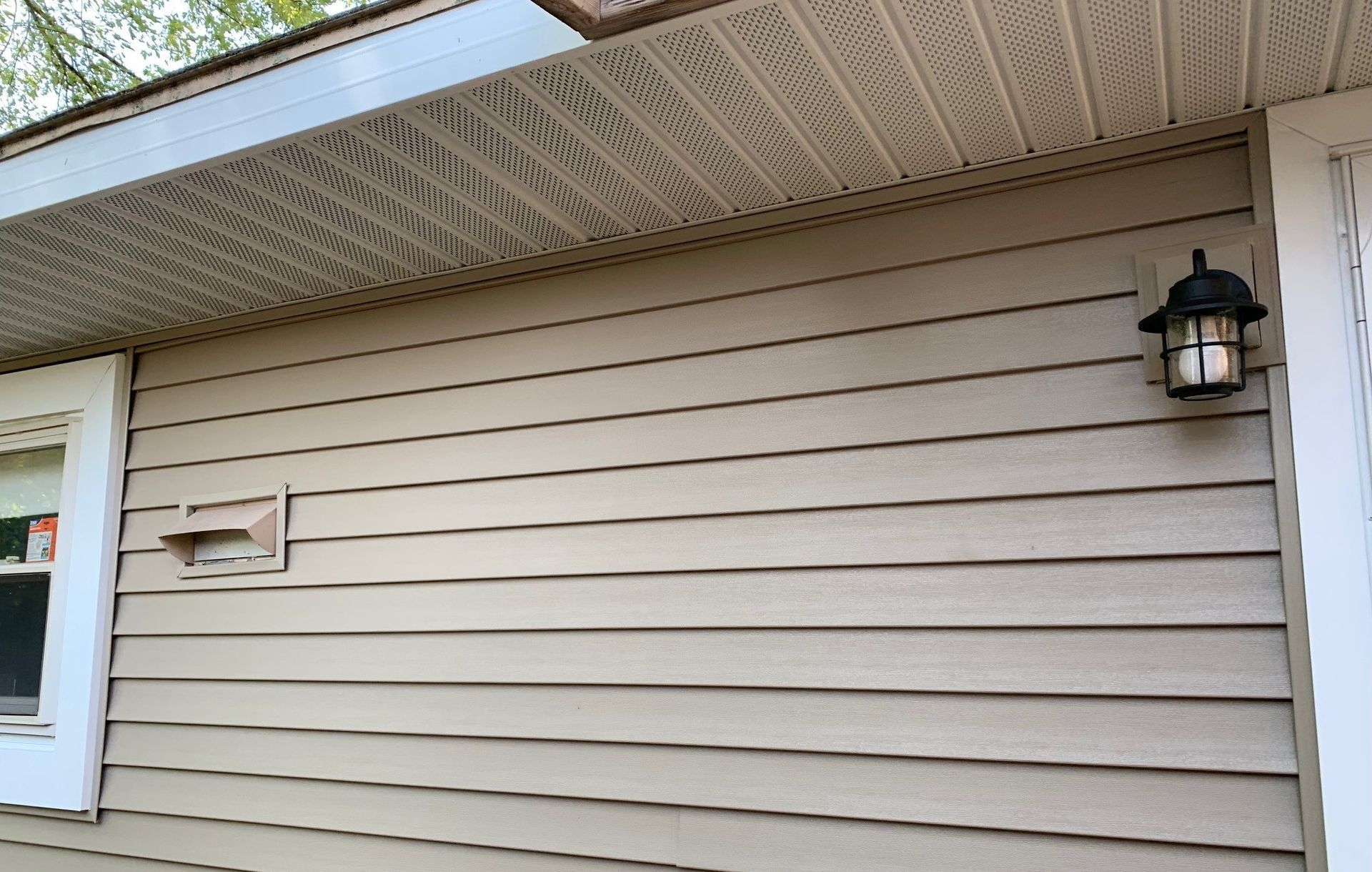Beige house siding with a black exterior wall lantern under the eaves.