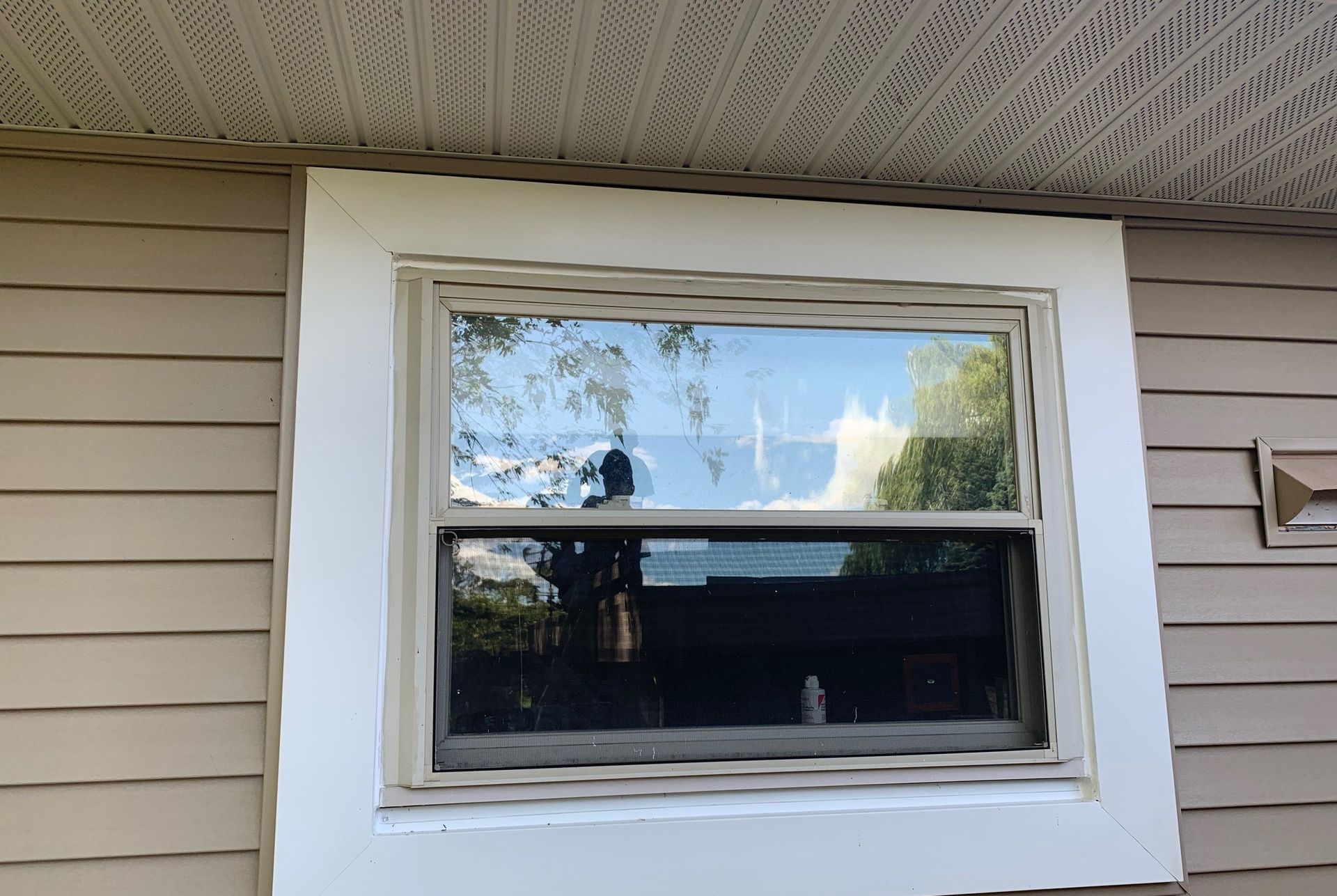 White house window with beige siding and tree reflections in the glass