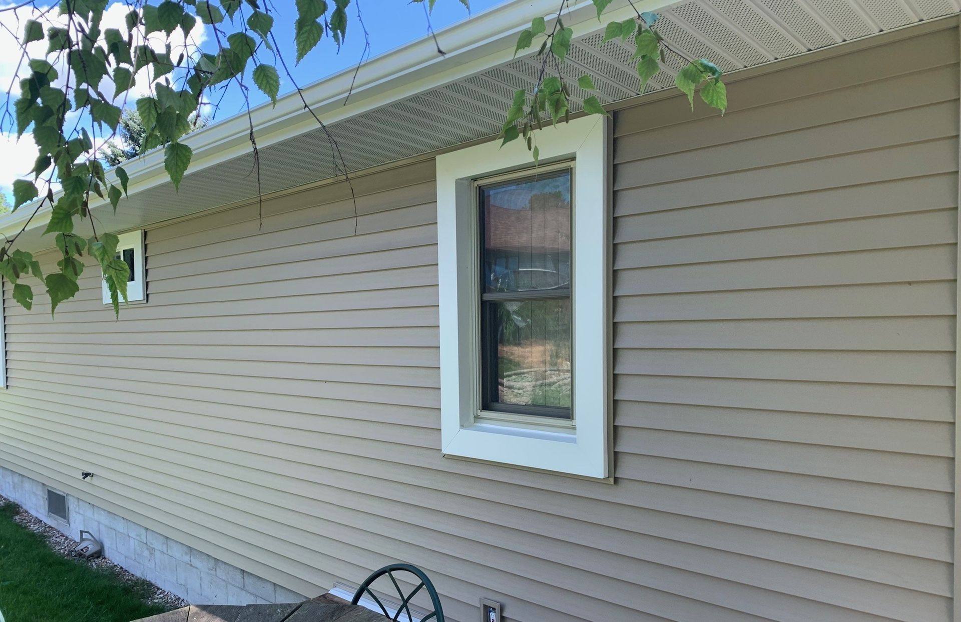 Tan-sided house exterior with a small window and white trim under a roof eave