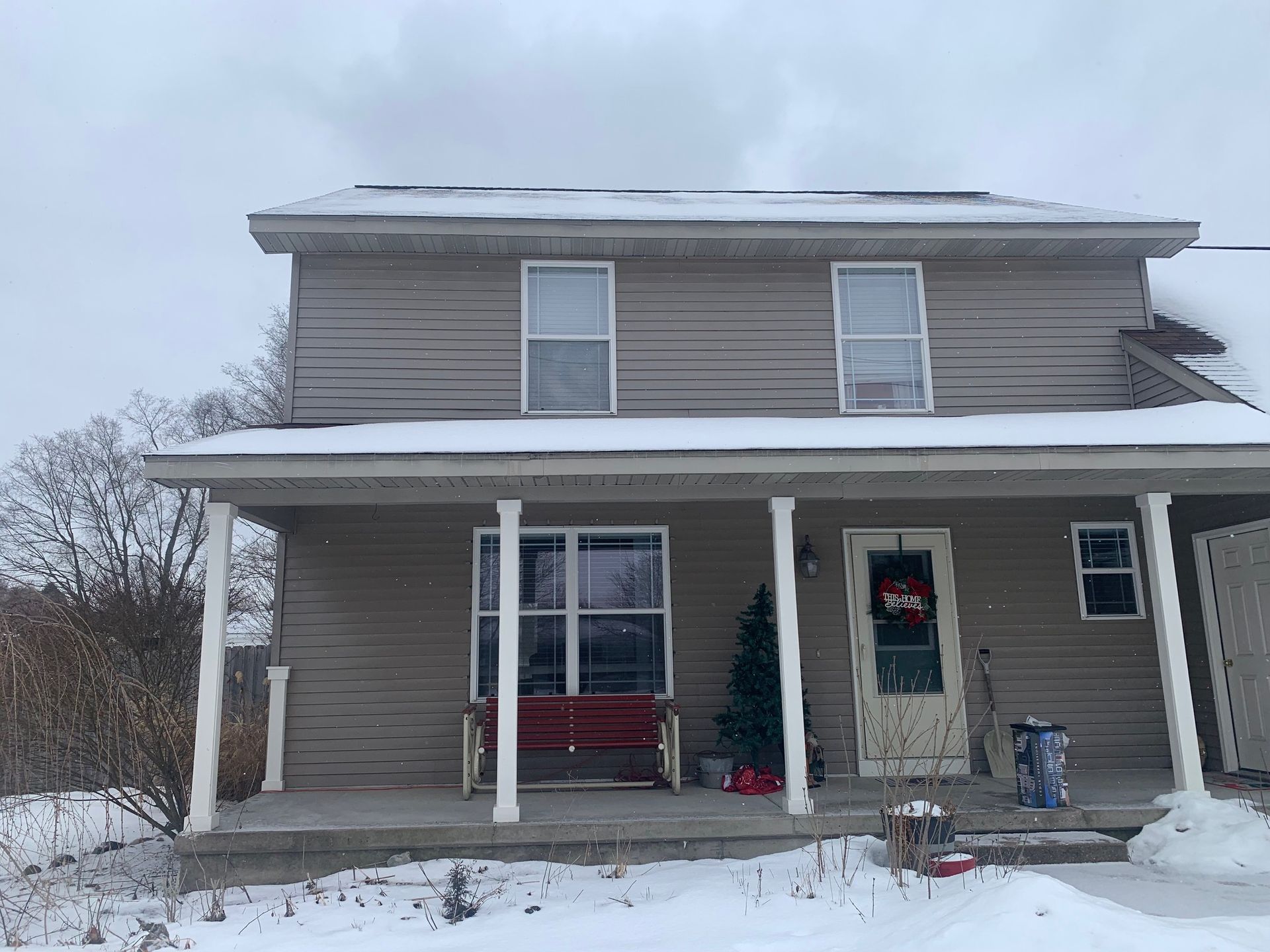 Snow-covered two-story house with gray siding, white trim, and a front porch under a winter sky