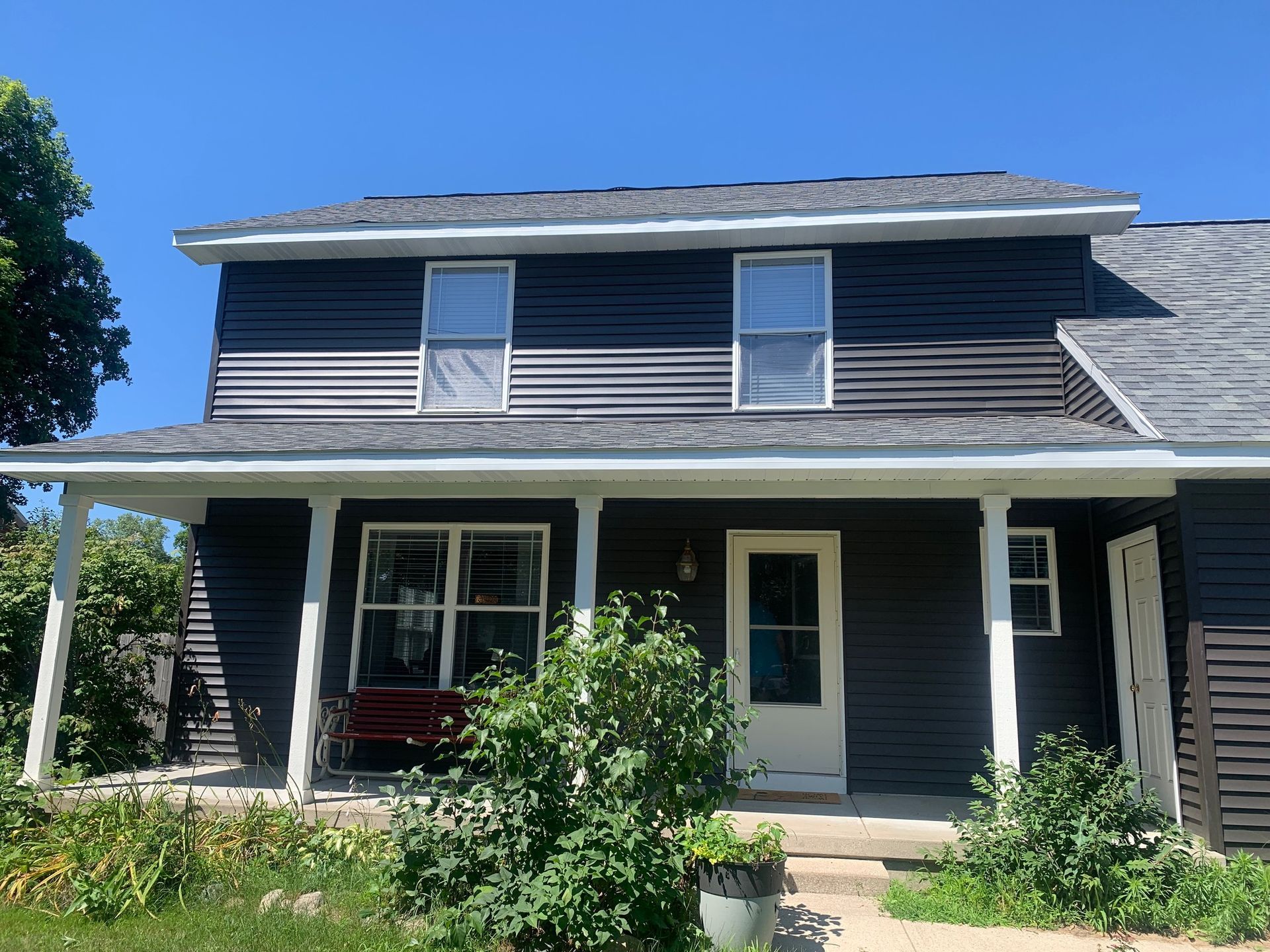 Two-story gray house with white trim, front porch, and a red bench under a clear blue sky