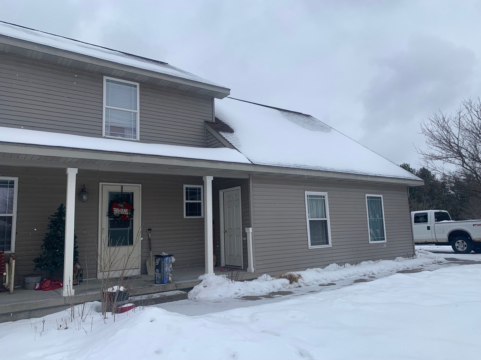 Snow-covered suburban house with beige siding, a front porch, and a white truck parked beside it.