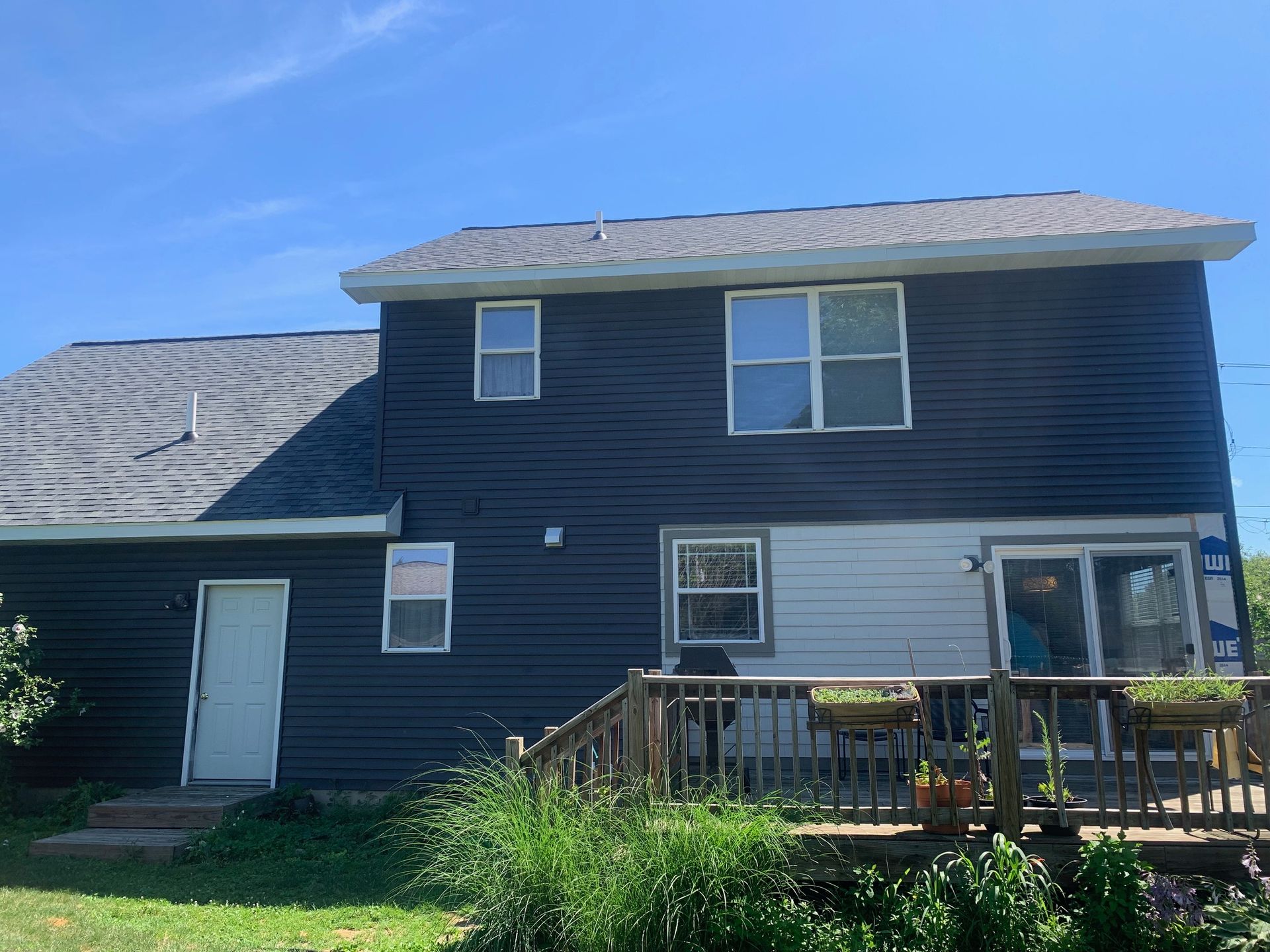 Dark blue two-story house with white trim, small deck, and a grassy yard under a clear sky