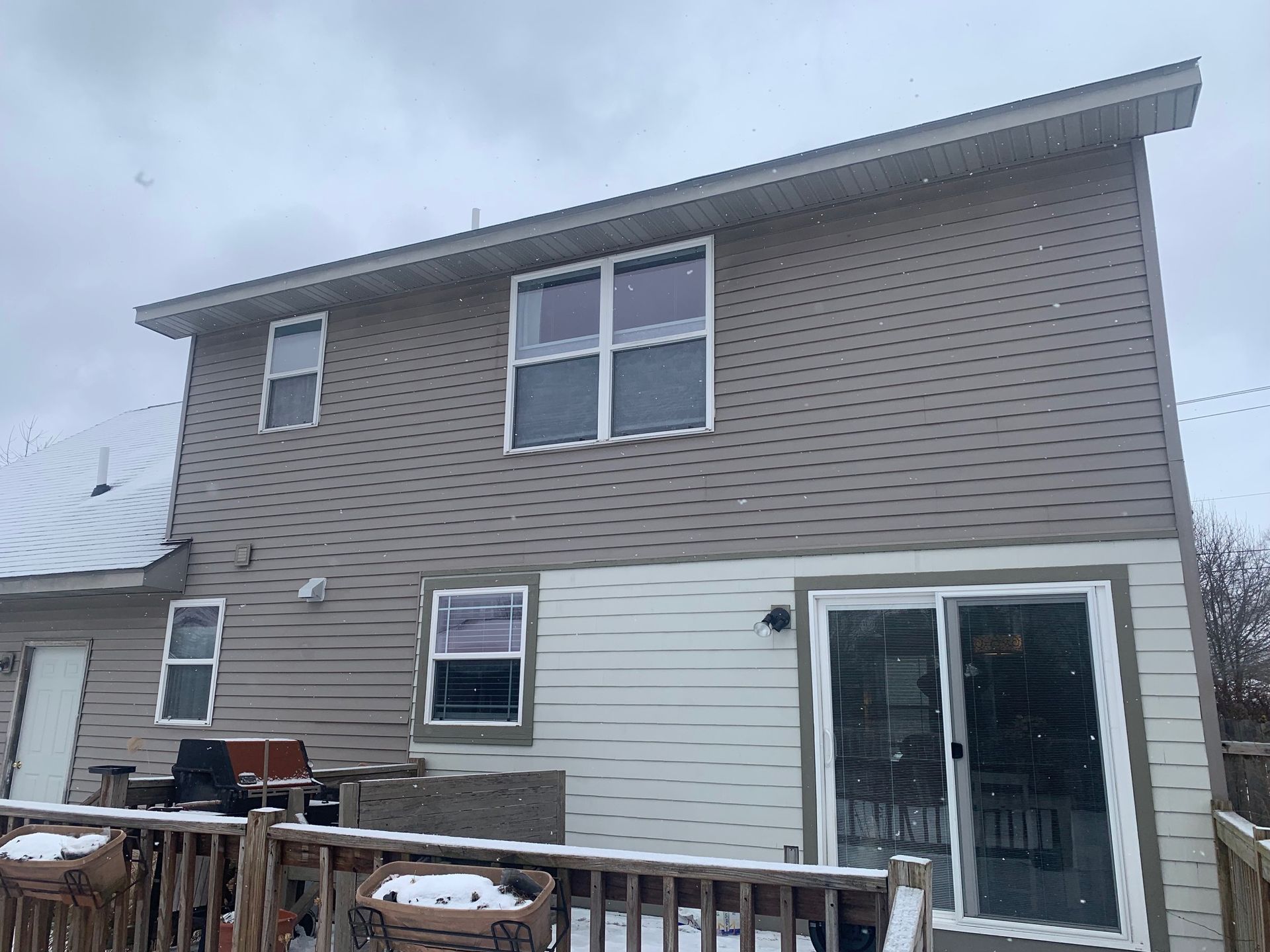 Snow-dusted two-story house with beige siding, white lower exterior, and a glass sliding door.