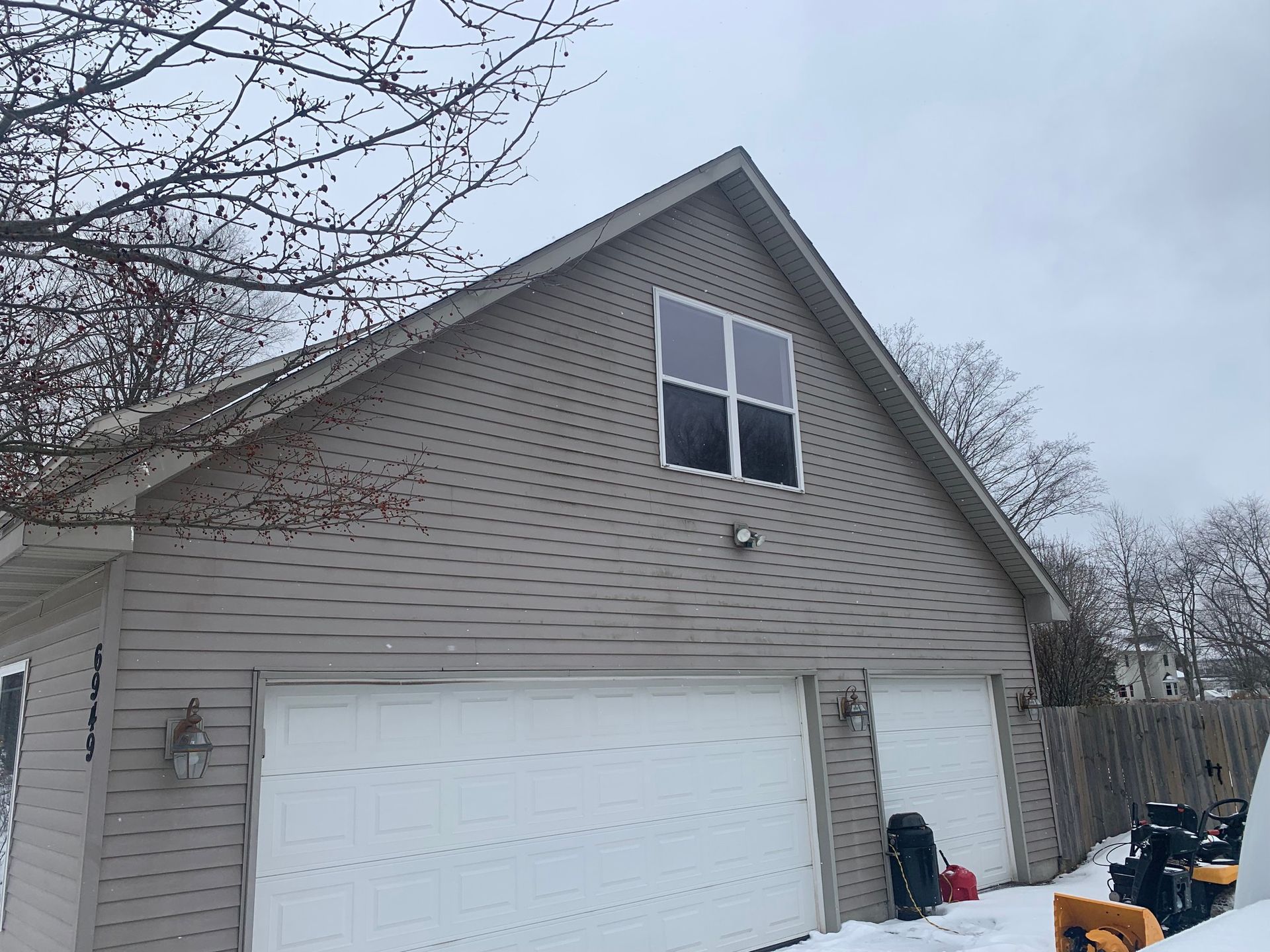 Two-story beige garage with white door and dormer windows in a snowy yard