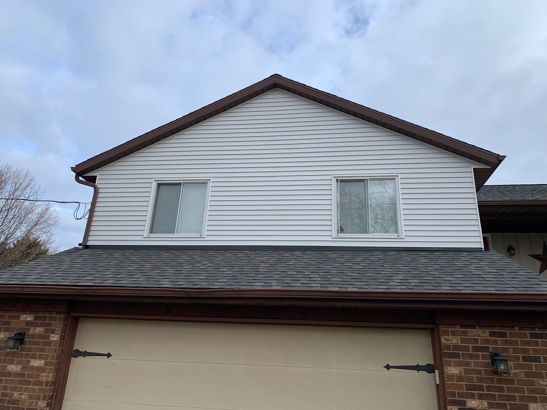 White two-story house exterior with brown trim and a beige garage door under a cloudy sky