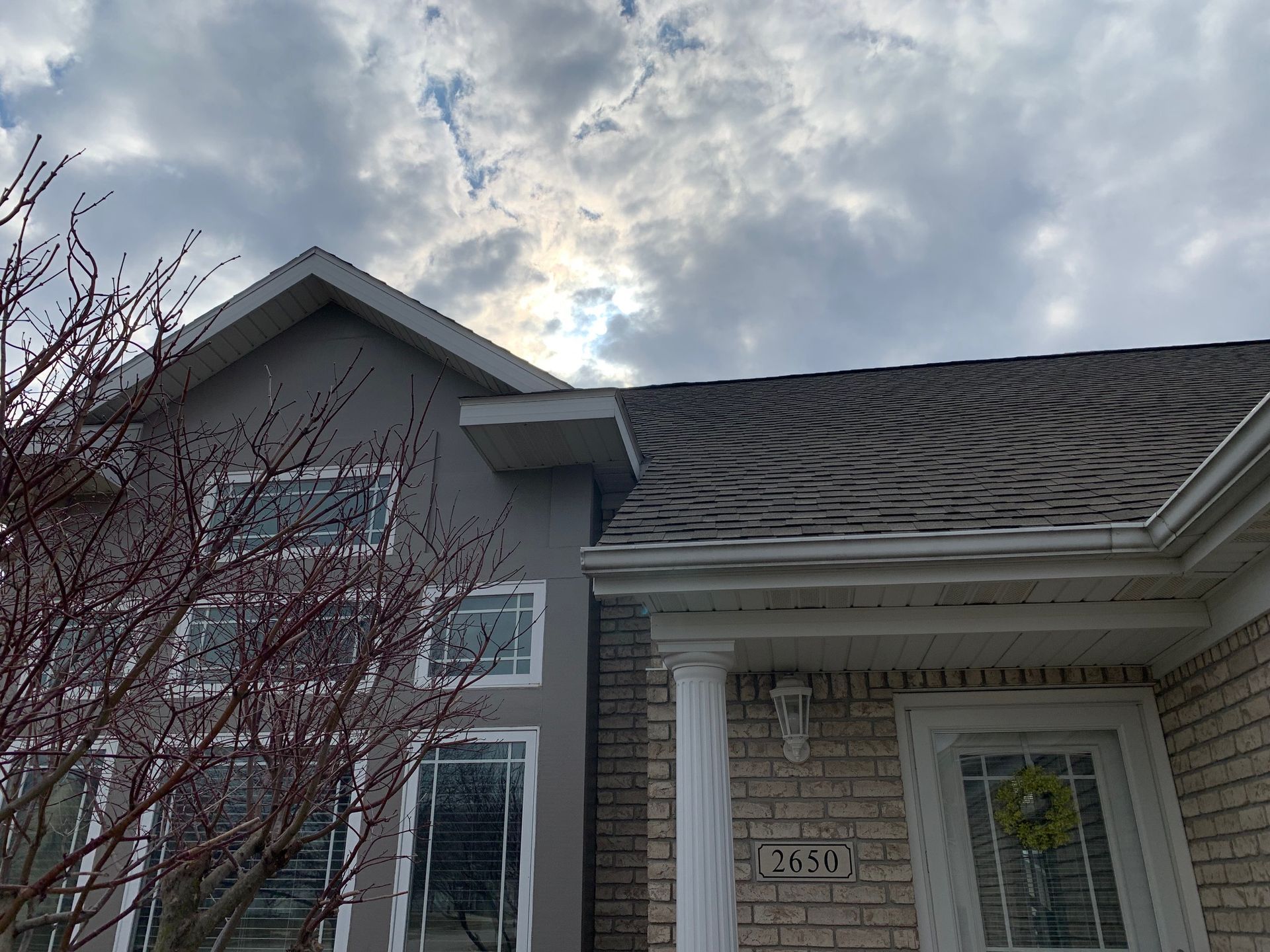 Front entrance of a gray house with white columns and a cloudy sky overhead