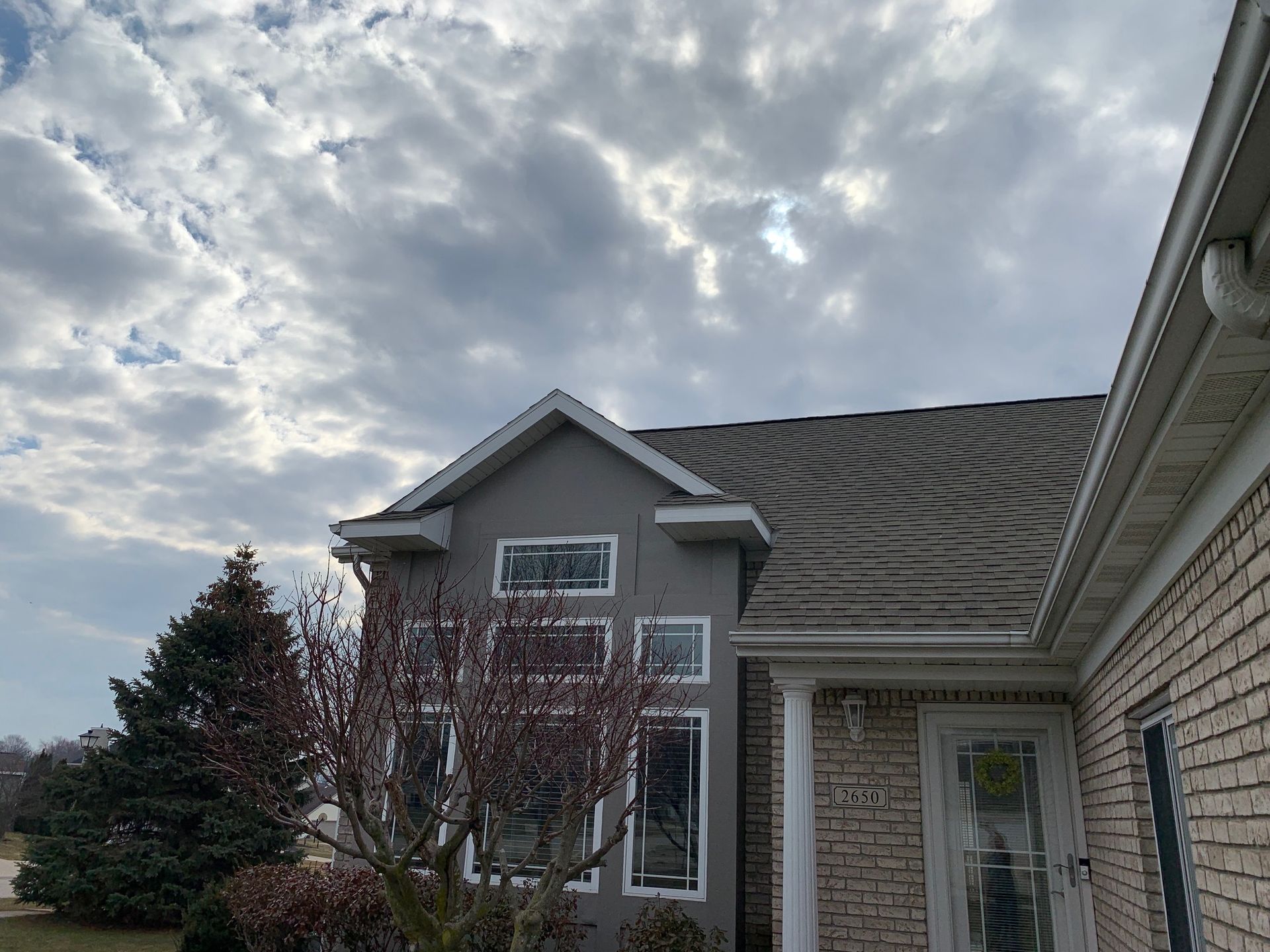 Suburban house exterior with gray siding, large windows, and cloudy sky overhead