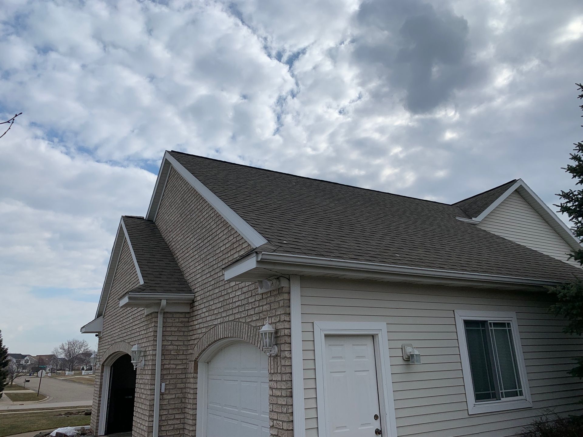 Suburban house exterior with beige siding, white trim, and a cloudy sky above
