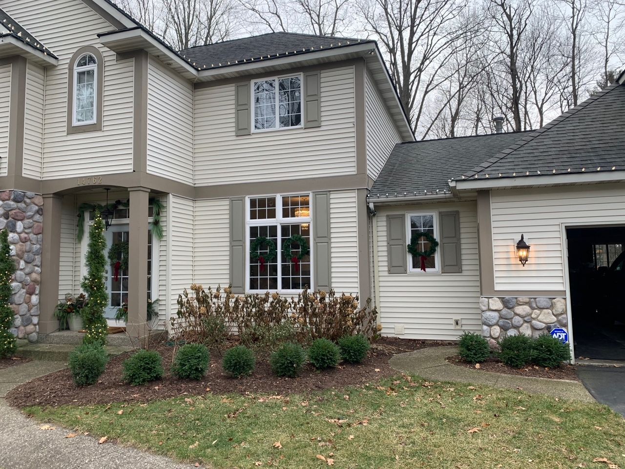 Suburban two-story house with beige siding, wreath on window, and garage visible on a cloudy day