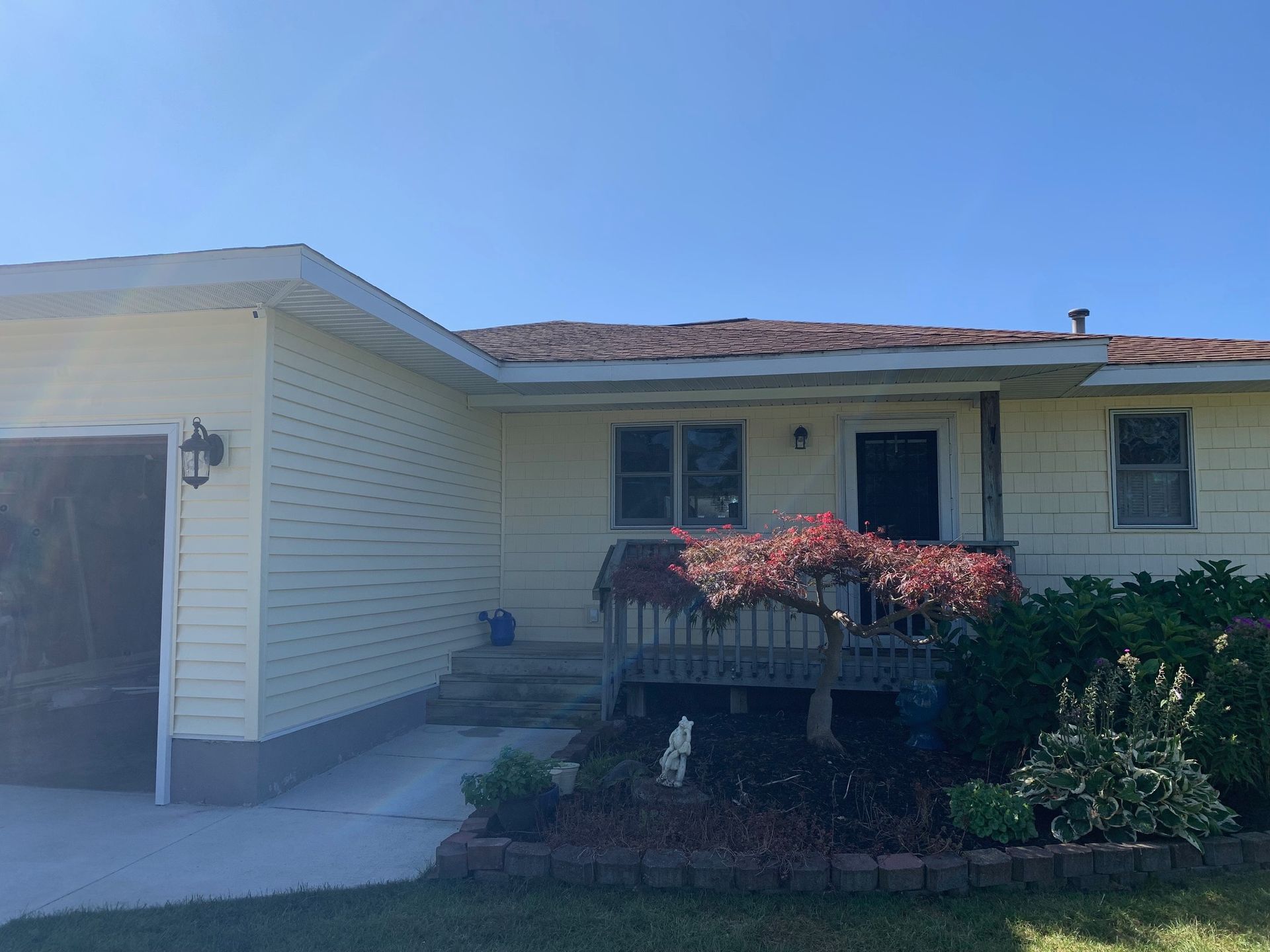 Single-story house exterior with white siding, red roof, and a front planter under a blue sky