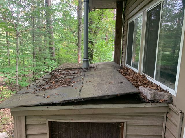 Collapsed roof on a small wooden shed beside a house, with trees in the background.
