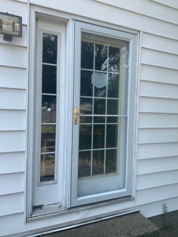White exterior door with narrow sidelight and brass handle on a house with light siding