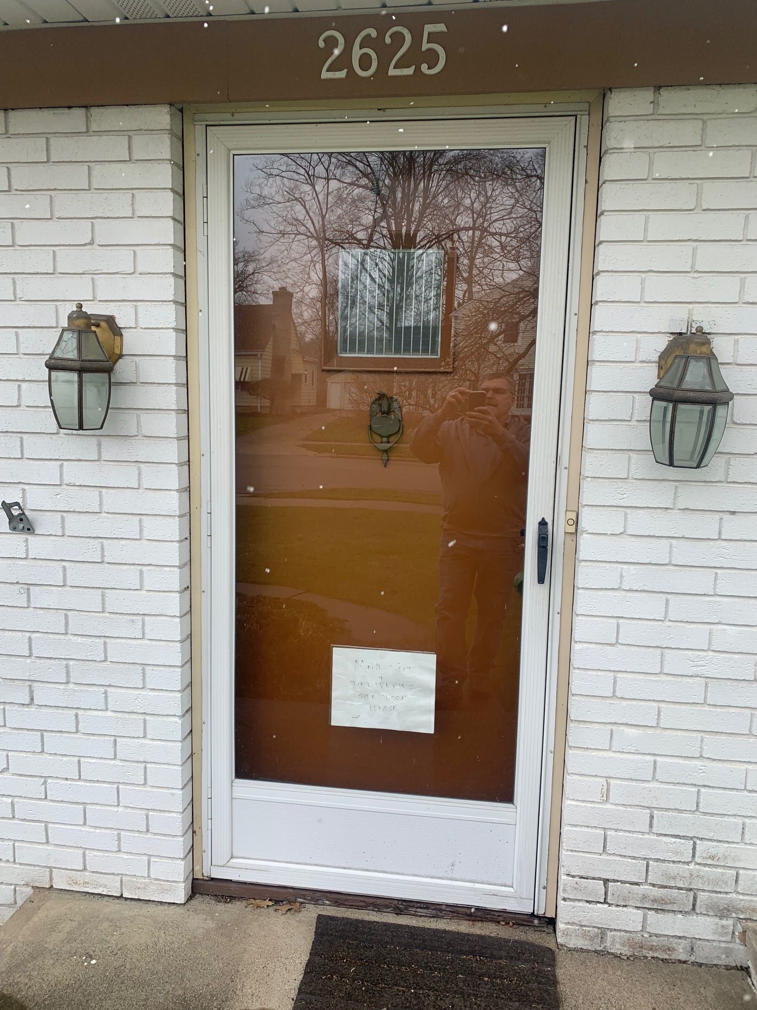 Front entrance with white brick walls, glass storm door, wall lanterns, and house number 2625 above.
