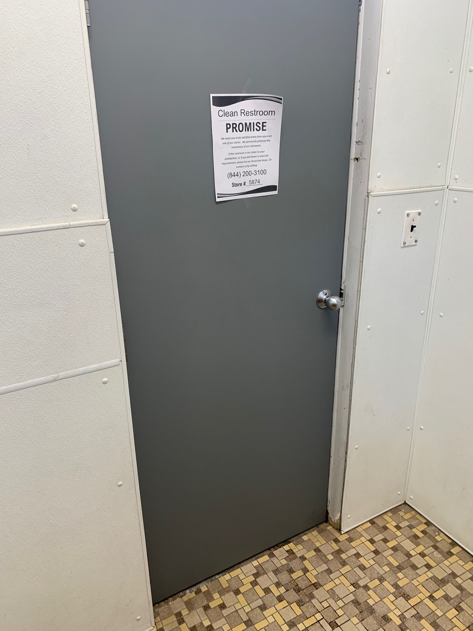 Gray door in a tiled hallway with a small sign on it.